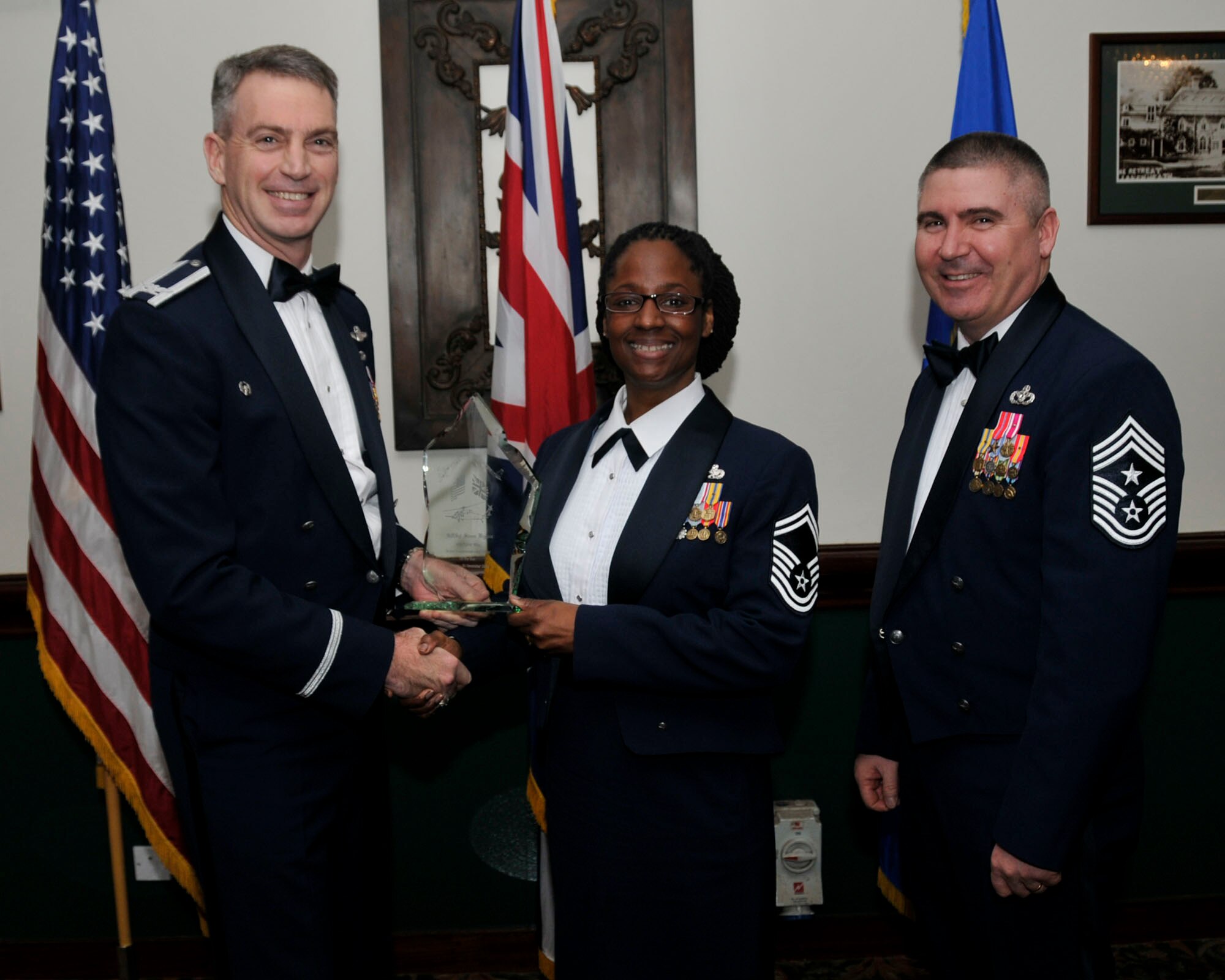 Col. Lawrence Reed, 48th Fighter Wing vice commander (left) and Chief Master Sgt. James Lucas present Senior Master Sgt. Iris Higgins on behalf of Senior Master Sgt. Steven Higgins, 48th Communications Squadron, with the award for Senior Non-Commissioned Officer of the Year at the annual awards at the Eagles Landing Feb 13. (U.S. Air Force photo by Airman 1st Class Eboni Knox)
