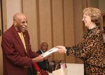 Local author Barbara Bir (right) presents Dr. Granville Coggs a copy of her book, "A 21-Story Salute," at the Air Force Village Feb. 9. The book tells the story of World War II veterans, including 15 residents of the Air Force Village and Dr. Coggs, a member of the Tuskegee Airmen. (U.S. Air Force photo/Robbin Cresswell)