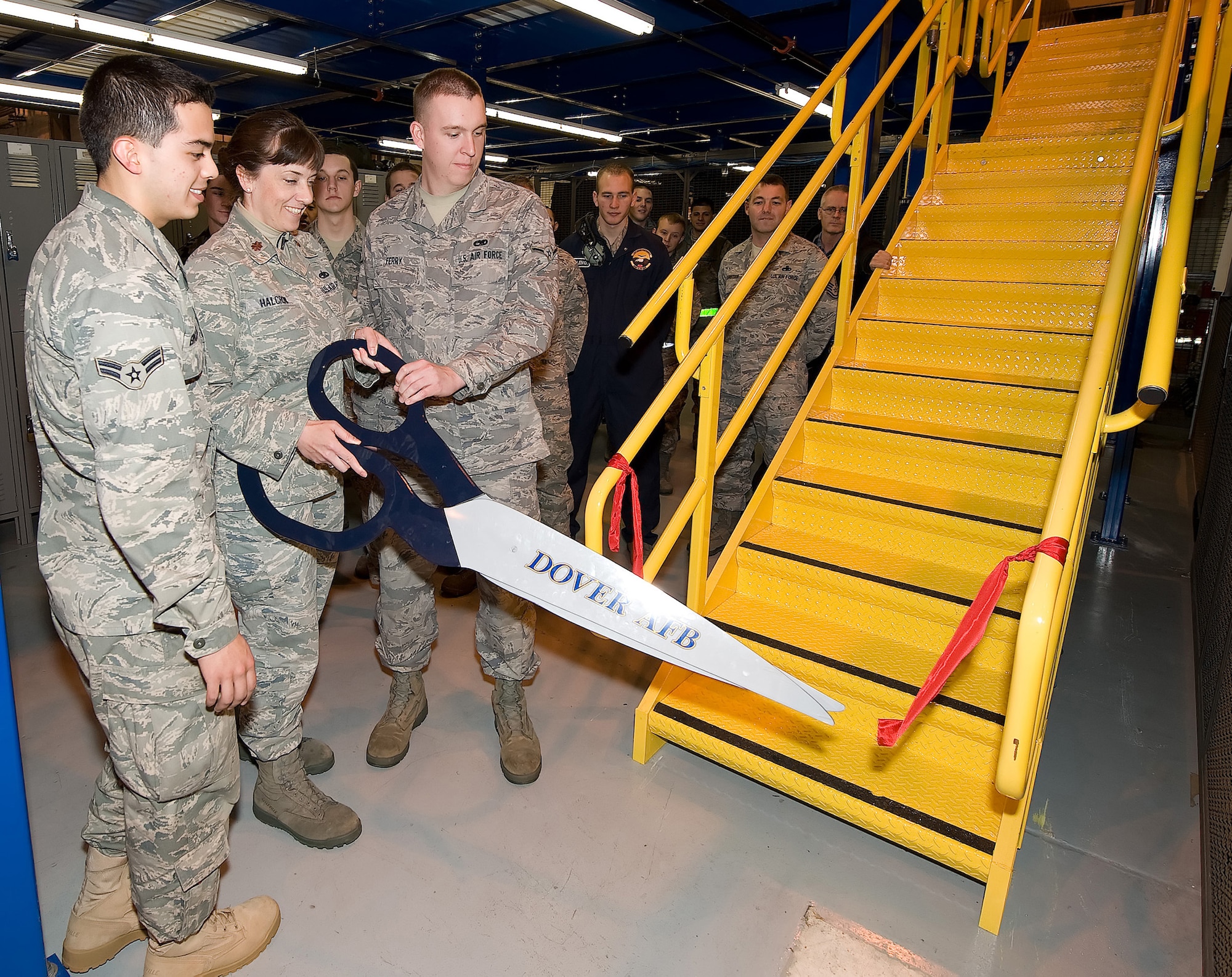 (From left) Airman 1st Class Jonathan Erickson and Airman Clifford Ferry, 436th Aircraft Maintenance Squadron members, help cut the ribbon to celebrate the squadron's recently built mezzanine installed with new lockers in Hangar 793. (U.S. Air Force photo/Jason Minto)