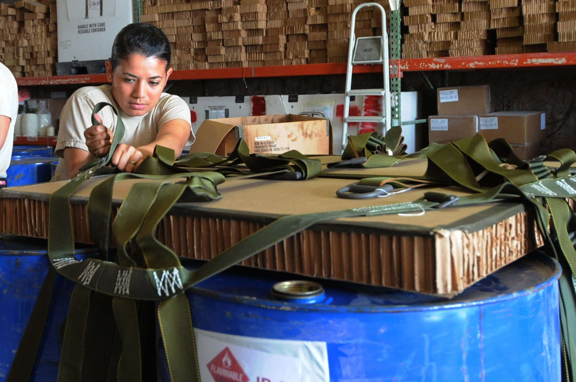 Army Spc. Diana Vegaprieto, 824th Riggers Detachment parachute rigger, tightens a sling assembly strap to an airdrop mission's container delivery system holding a cargo of four 55-gallon drums of JP-8 fuel  at a non-disclosed Southwest Asia location, Feb 16, 2010. (U.S. Air Force photo by Tech. Sgt. Michelle Larche)[RELEASED]