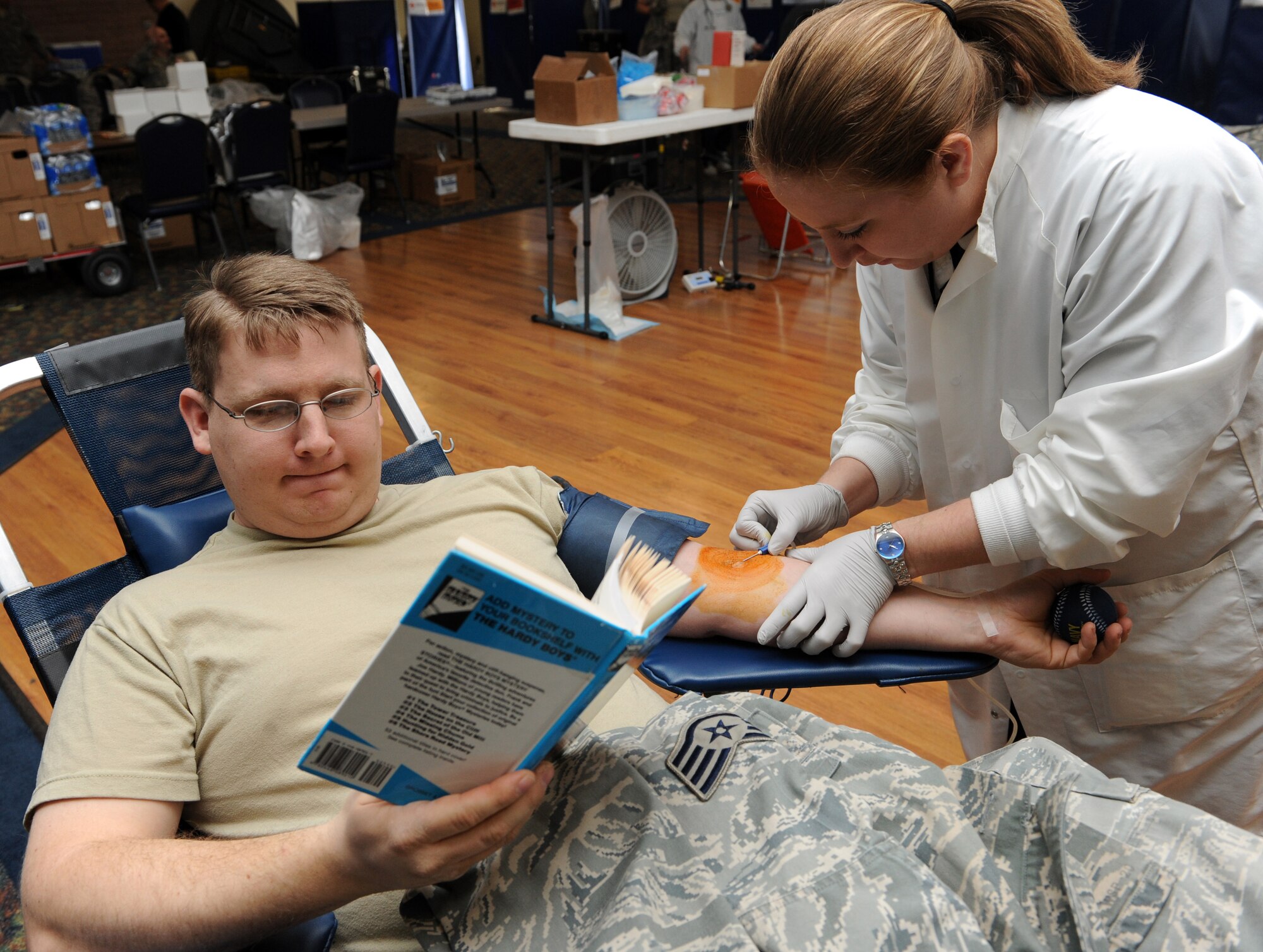MOUNTAIN HOME AIR FORCE BASE, Idaho -- Staff Sgt. Erin Packer, 366th Ammunitions Flight storage crew chief, reads a book as Shaunna Allen, Red Cross phlebotomist, draws blood from his arm during a blood drive at the community center Feb. 11. According to www.redcrossblood.org, the American Red Cross holds more than 200,000 blood drives every year. (U.S. Air Force photo by Airman 1st Class Debbie Lockhart)