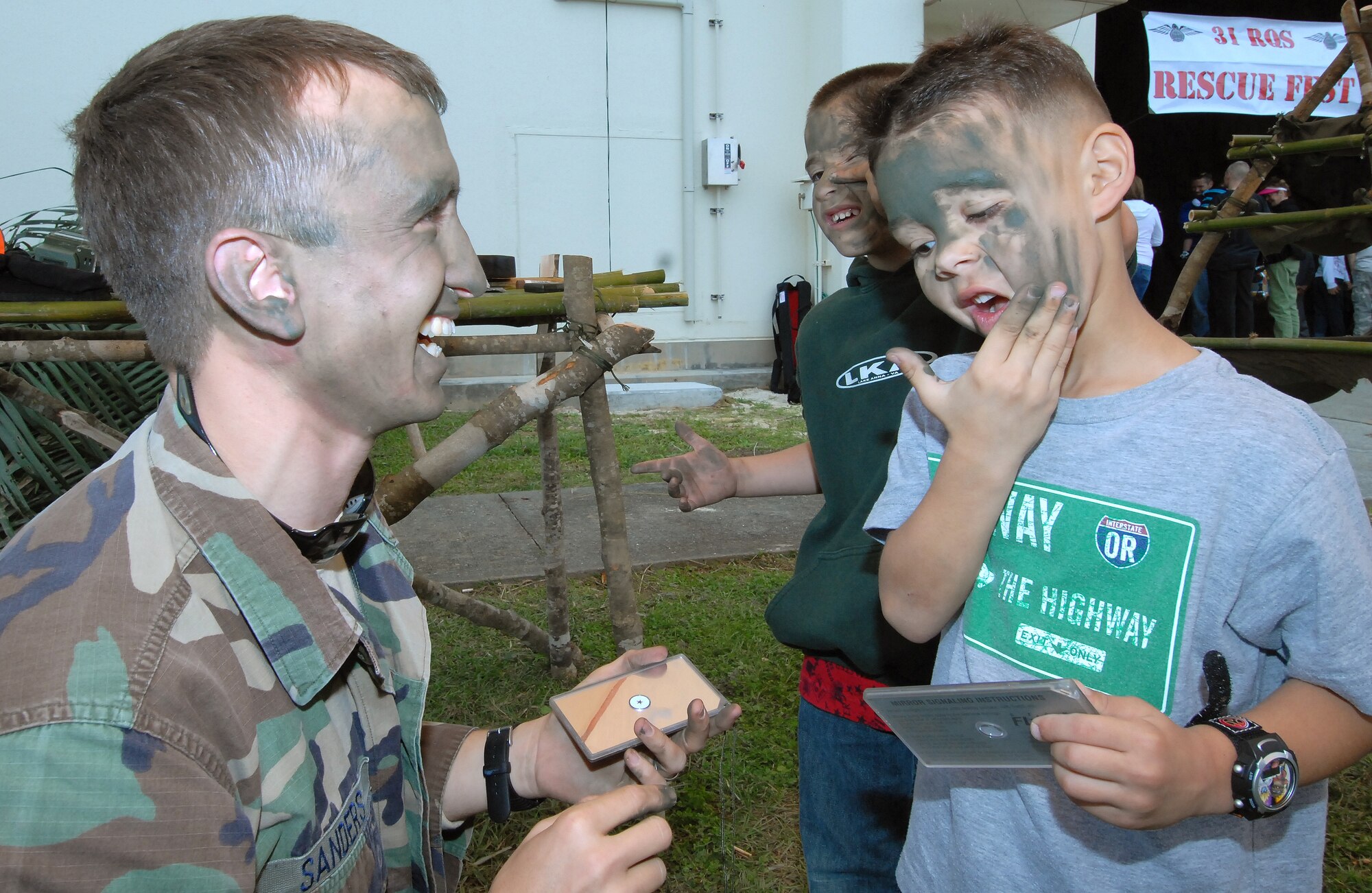 Staff Sgt. Aaron Sanders, 31st Rescue Squadron Survival, Escape, Resistance and Evasion specialist, helps Sean Nissel and Leo Salinas IV apply camoflage during Rescue Fest Feb. 20. Hundreds of servicemembers and families visited the 31st RQS to watch demonstrations and talk with Airmen in the unit about how they contribute to the Air Force mission. (U.S. Air Force photo/Staff Sgt. Jason Lake)