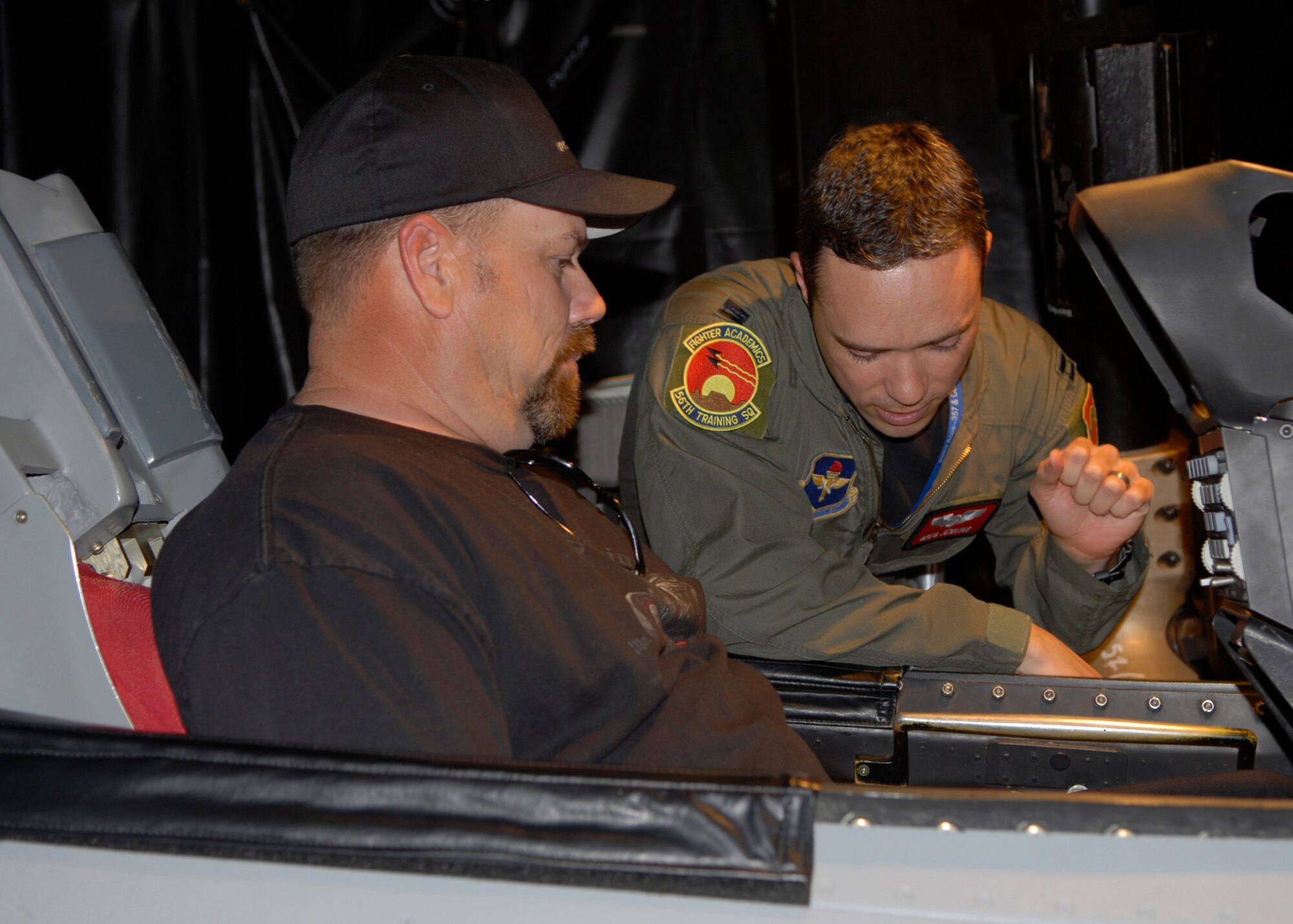 Capt. Gregory Jenkins, 56th Training Squadron instructor pilot, teaches Branden Hyslope how to operate an F-16 in the simulator during a tour Feb. 9. Mr. Hyslopes wife, Jamie Hyslope, is a patient at Cancer Treatment Centers of America who competed against him in the simulator. (U.S. Air Force photo by Airman 1st Class Ronifel Yasay)