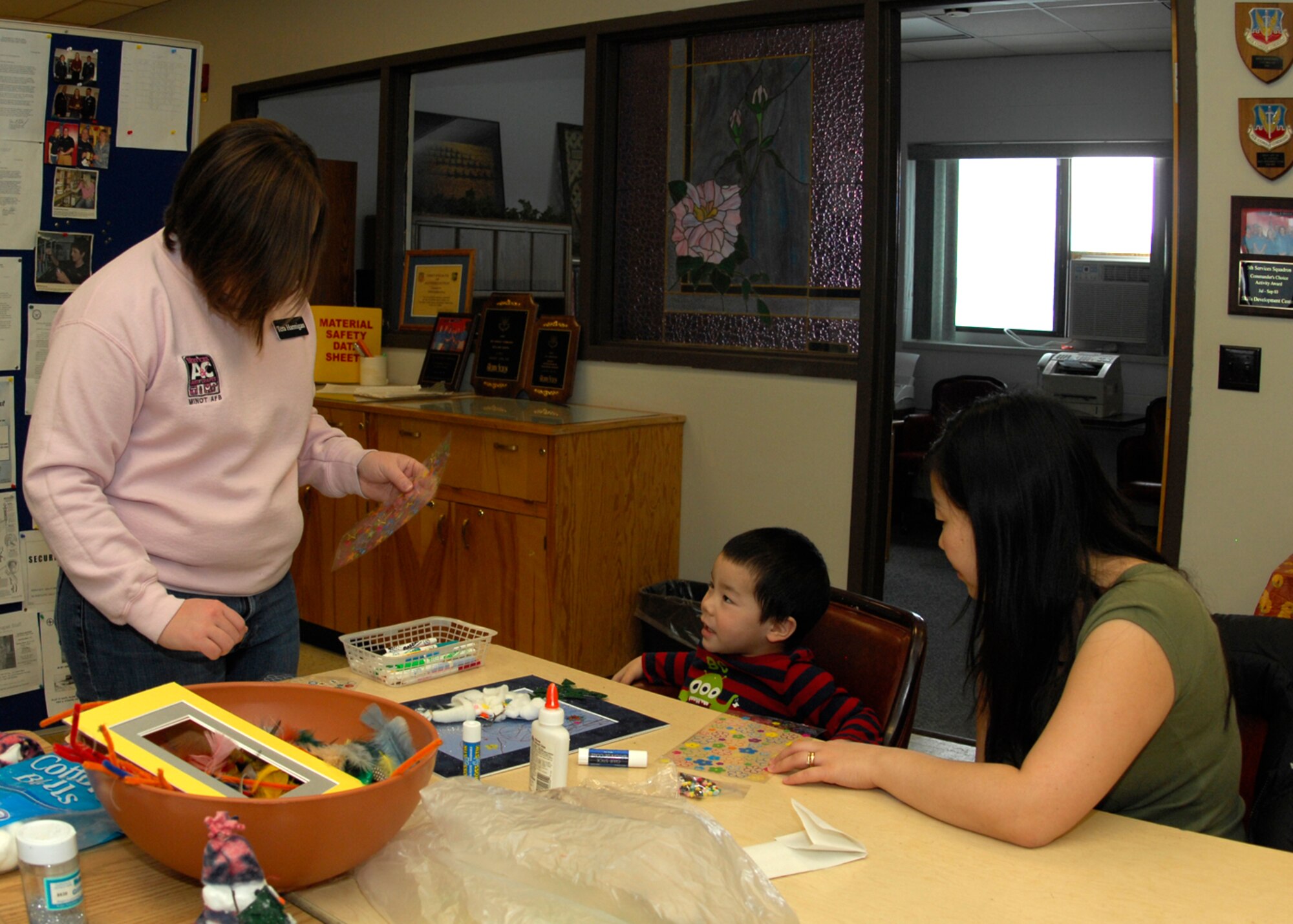MINOT AIR FORCE BASE, N.D. – Mrs. Tera Hannigan, arts and crafts class instructor and spouse of Capt. Joseph Hannigan, 91st Operations Support Squadron ICBM senior combat crew commander instructor, helps Roman Slajchert, son of Staff Sgt. Jason Slajchert 5th Medical Operations Squadron medical technician, pick out stickers while his mother, Mrs. Carla Slajchert, observes. With help from his mother and instructor, Roman made a creative picture of a snowman in a wintery wonderland. (U.S. Air Force photo by Airman 1st Class Ashley N. Avecilla)