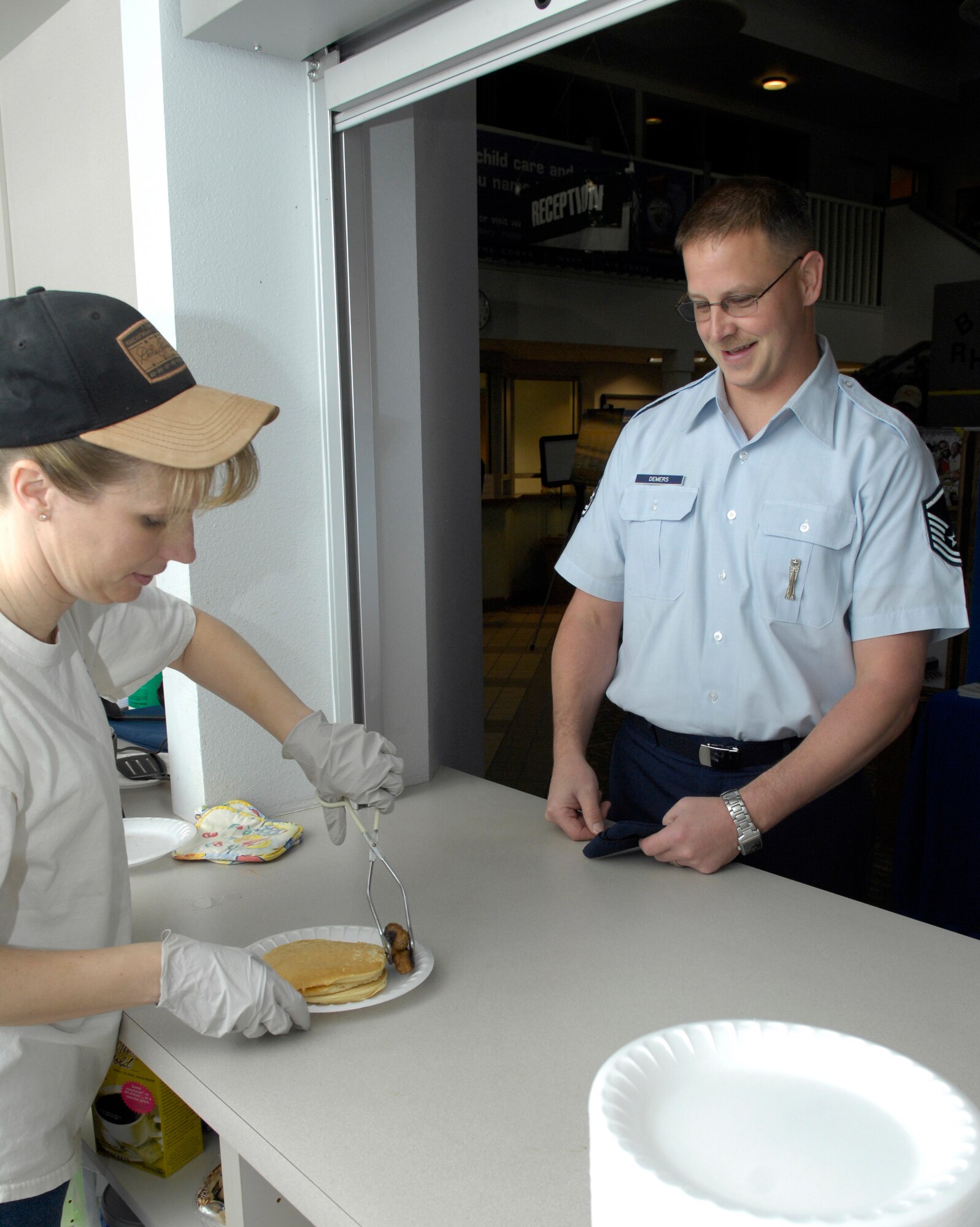 VANDENBERG AIR FORCE BASE, Calif. -- Master Sgt. Robert Demers, of the 30th Launch Group, watches as Master Sgt. Minnette Bohlander, also of the 30th LCG, places sausage on his plate during the First Sergeants' Pancake Breakfast hosted by the Airman and Family Readiness Center here Monday, Feb. 22, 2010. The breakfast was used in conjuncture with the Military Saves Week, which urged Airman to protect their moneys and investments. (U.S. Air Force photo/Airman 1st Class Lael Huss)