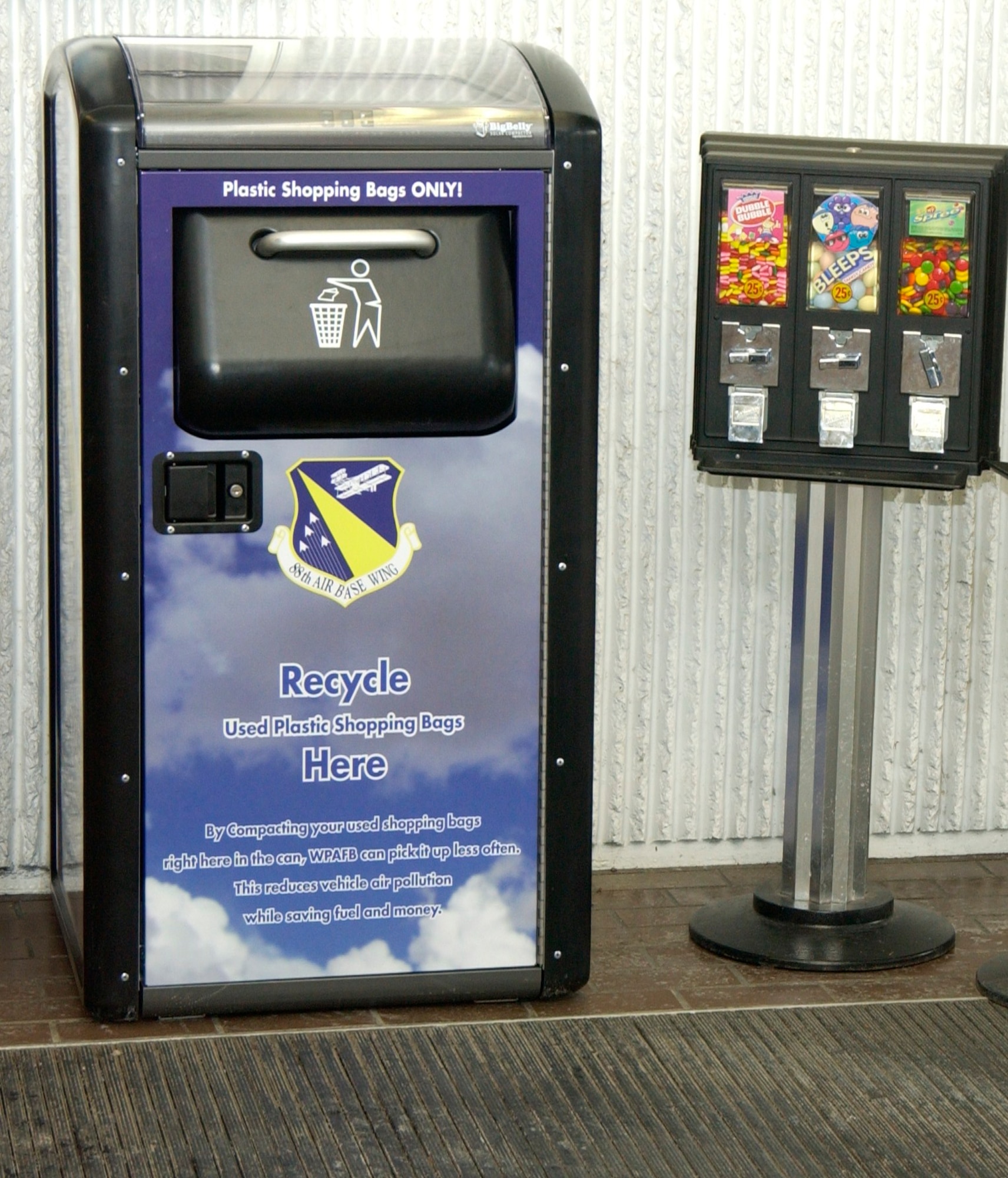 What's new in the entrance of the base Commissary?  Hint - it's not the candy machines.  It's the new solar plastic bag recycling machine compactor.  Wright-Patterson AFB now has three solar plastic bag recycling machines for people to discard their plastic bags which helps the base with recycling and stops filling up local landfills. (U.S. Air Force photo by Ted Theopolos)