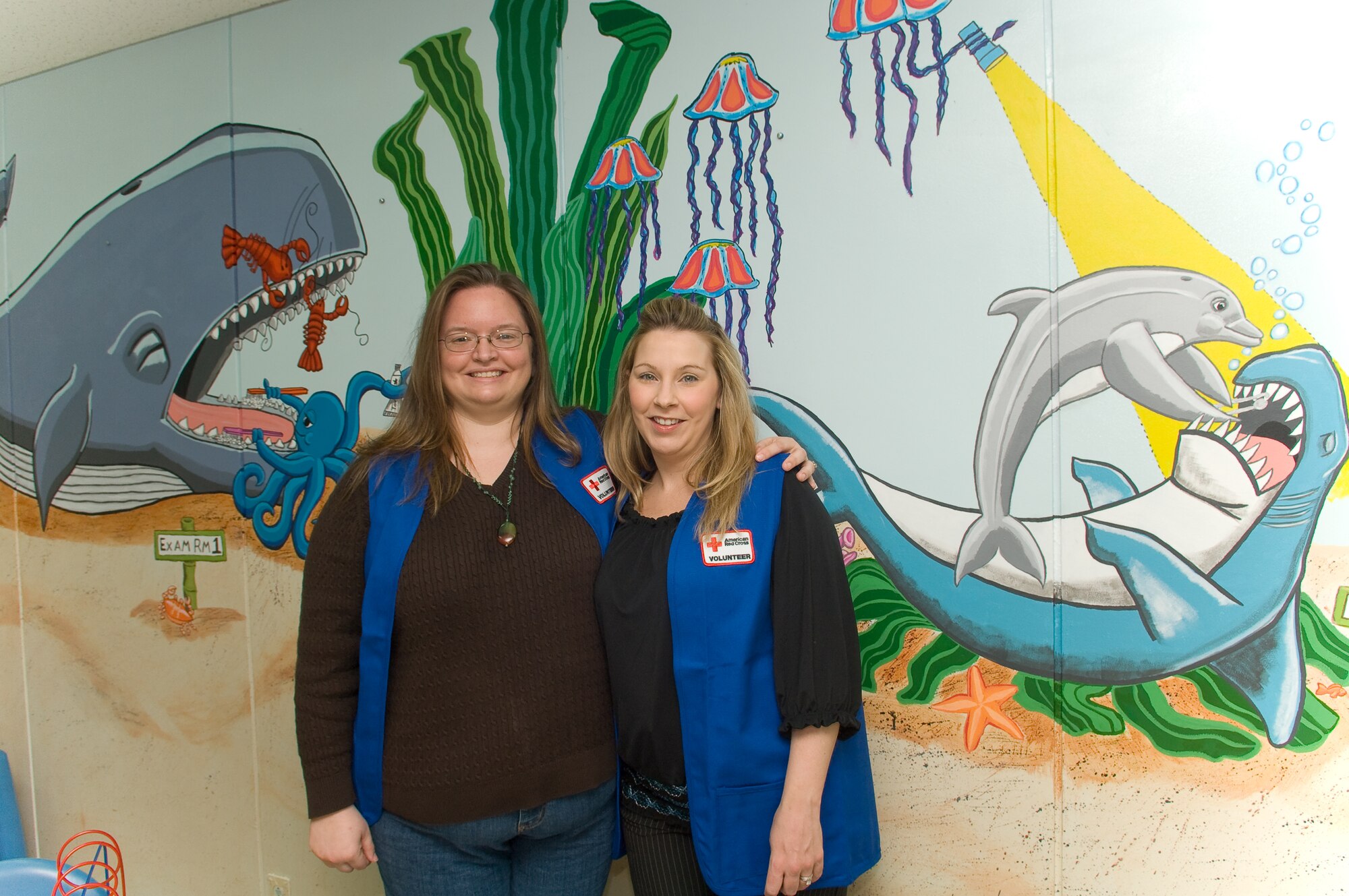 YOKOTA AIR BASE, Japan -- Mrs. Kelley Monkevich (left) and Mrs. Angela Rainey (right) stand in front of their mural painted on a wall at the 374th Dental clinic children's waiting room, here, Feb. 26. Mrs. Monkevich and Mrs. Reainey spent more than 100 hours paining on the wall and refurinishing the waiting room. (U.S. Air Force photo/Osakabe Yasuo)