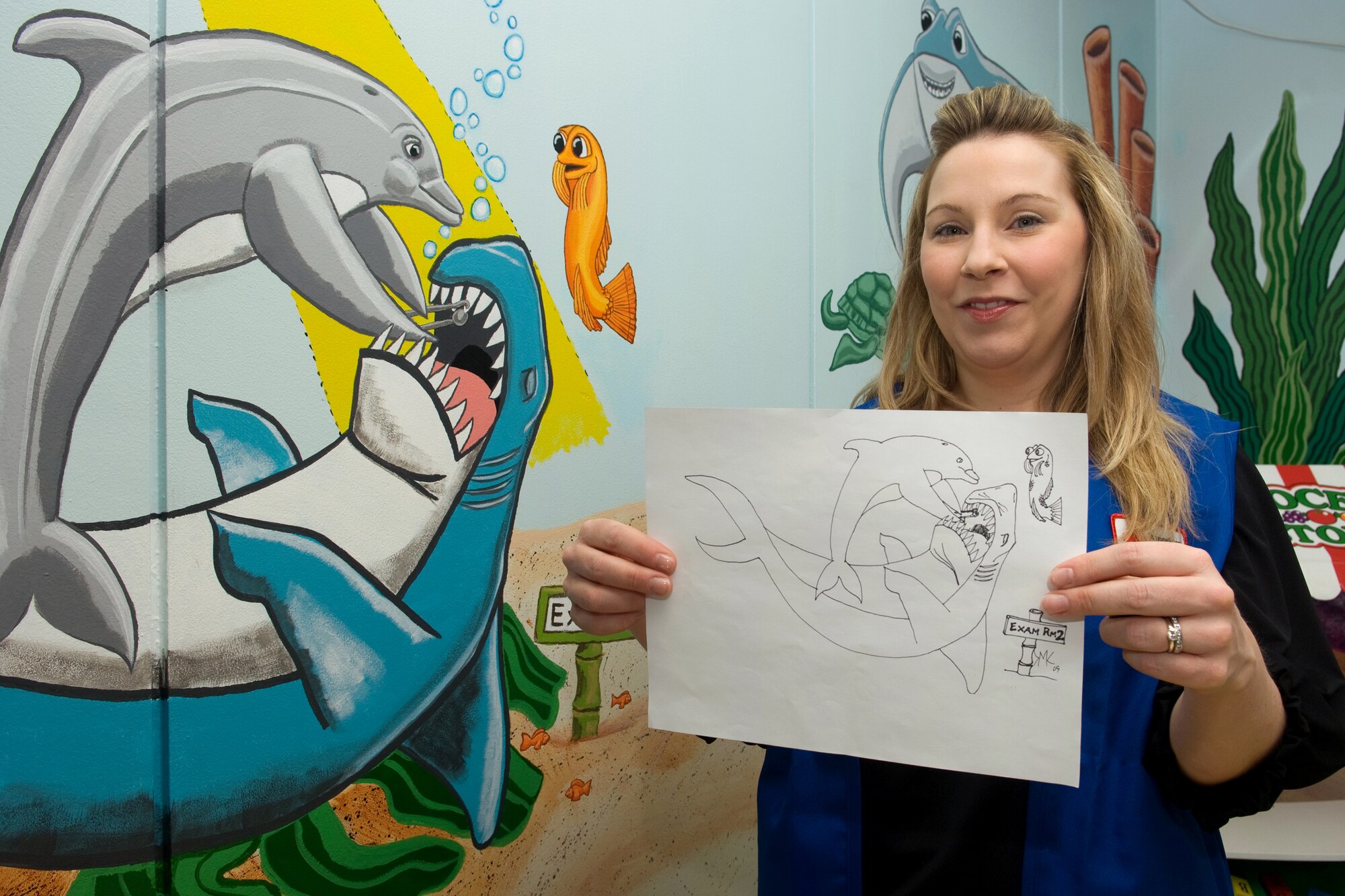 YOKOTA AIR BASE, Japan -- -- Mrs. Angela Rainey, American Red Cross volunteer, shows off her original drawing used to create part of a mural on a wall at the 374th Dental clinic children's waiting room, here, Feb. 26.  Mrs. Monkevich worked more than 100 hours painting and refurnishing the children’s waiting room at the dental clinic. (U.S. Air Force photo/Osakabe Yasuo)