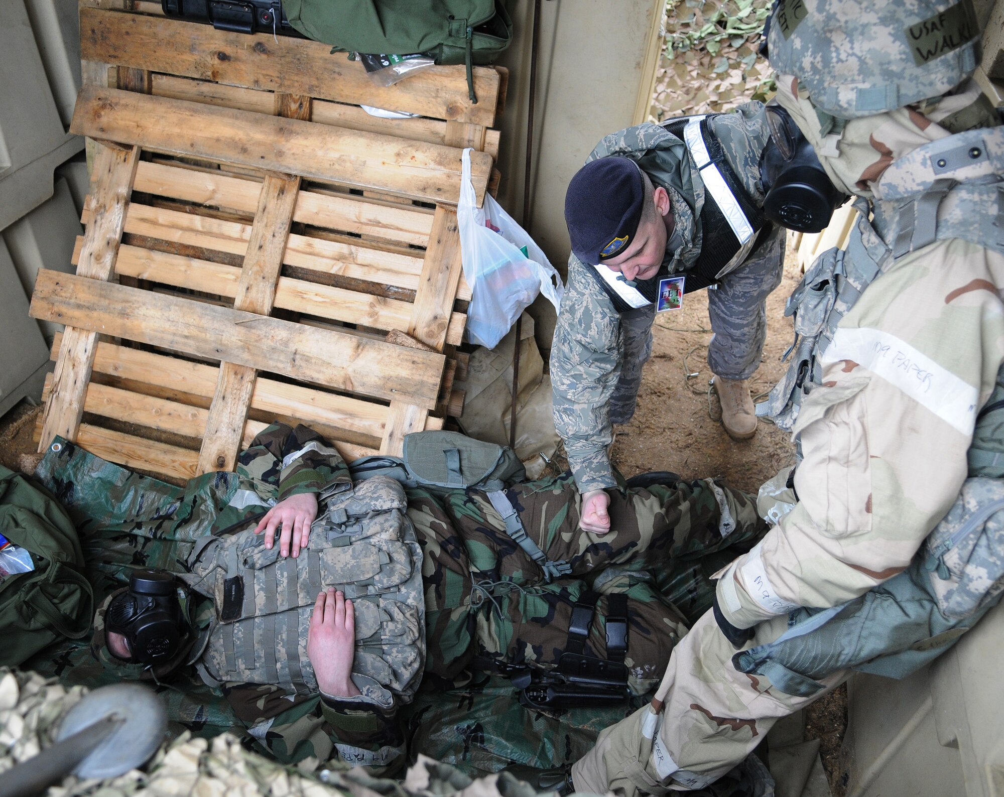 RAF MILDENHALL, England -- Master Sgt. John Carter, 100th Security Forces Squadron exercise evaluator (center) corrects Airman 1st Class Garrett Walker, 100th SFS (right), on the application of a chemical warfare antidote Feb. 25. Amn. Kyle Butters, 100th SFS, was "wounded" during an attack on Base X as part of an operational readiness exercise. (U.S. Air Force photo/Senior Airman Thomas Trower) 