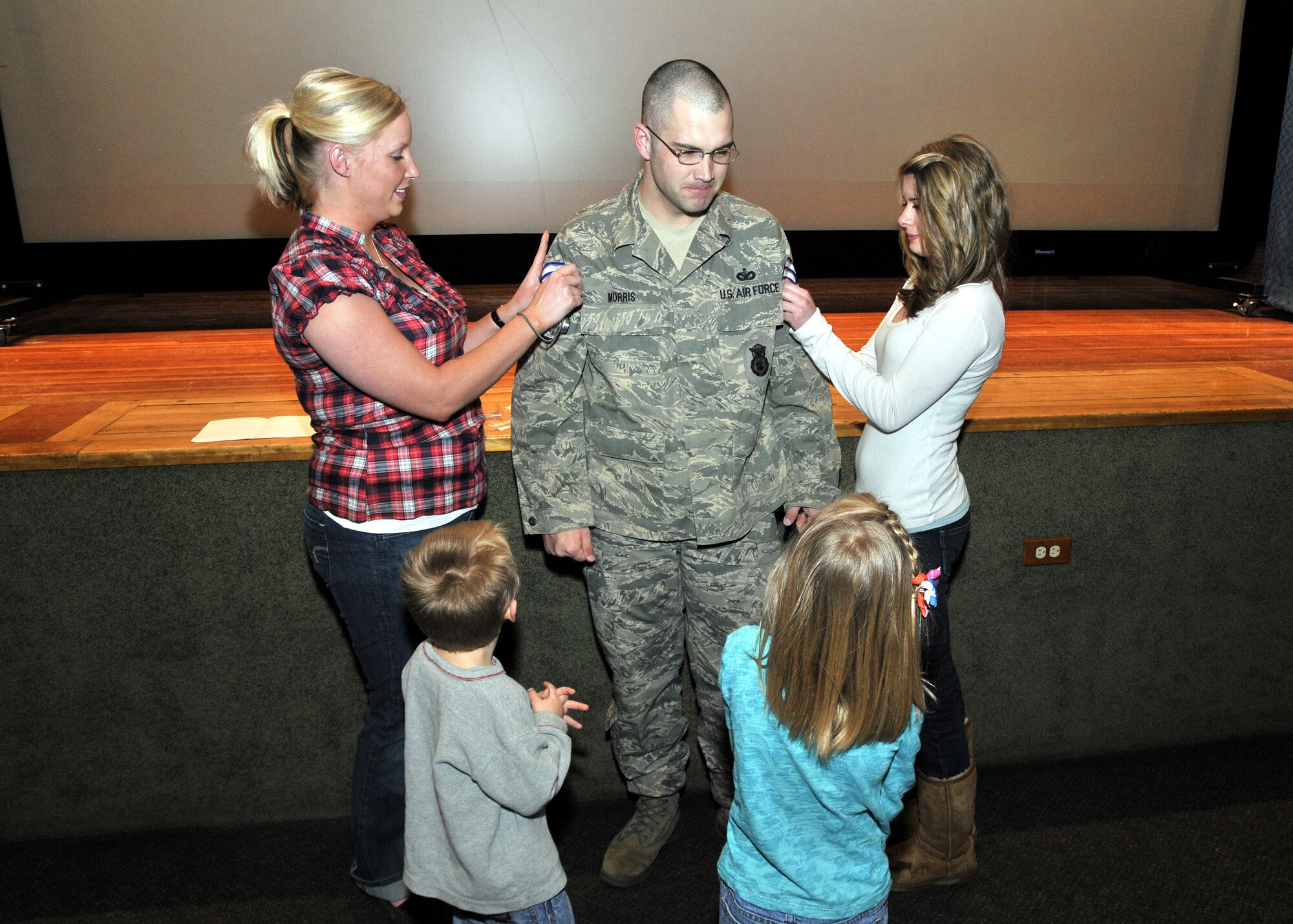 Tech. Sgt.  Derrik Morris gets his new "stripes" tacked on by his wife, Erin (left), and their German foreign exchange student Marie Wehinger, during a STEP promotion Feb. 18.  His children Jacob, 3, and Summerlin, 5, look on. (U.S. Air Force photo/John Turner)