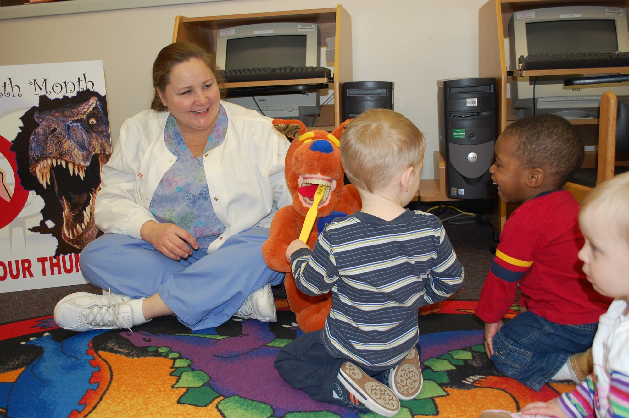 Dental technician Mercy Padgett works the kangaroon's mouth while preschoolers attending story hour at the library practice brushing the animals teeth during an educational session in honor of Children's Dental Health Month. Members of the Dental Clinic also visited the child development and youth centers. (U.S. Air Force photo/Valerie Mullett)