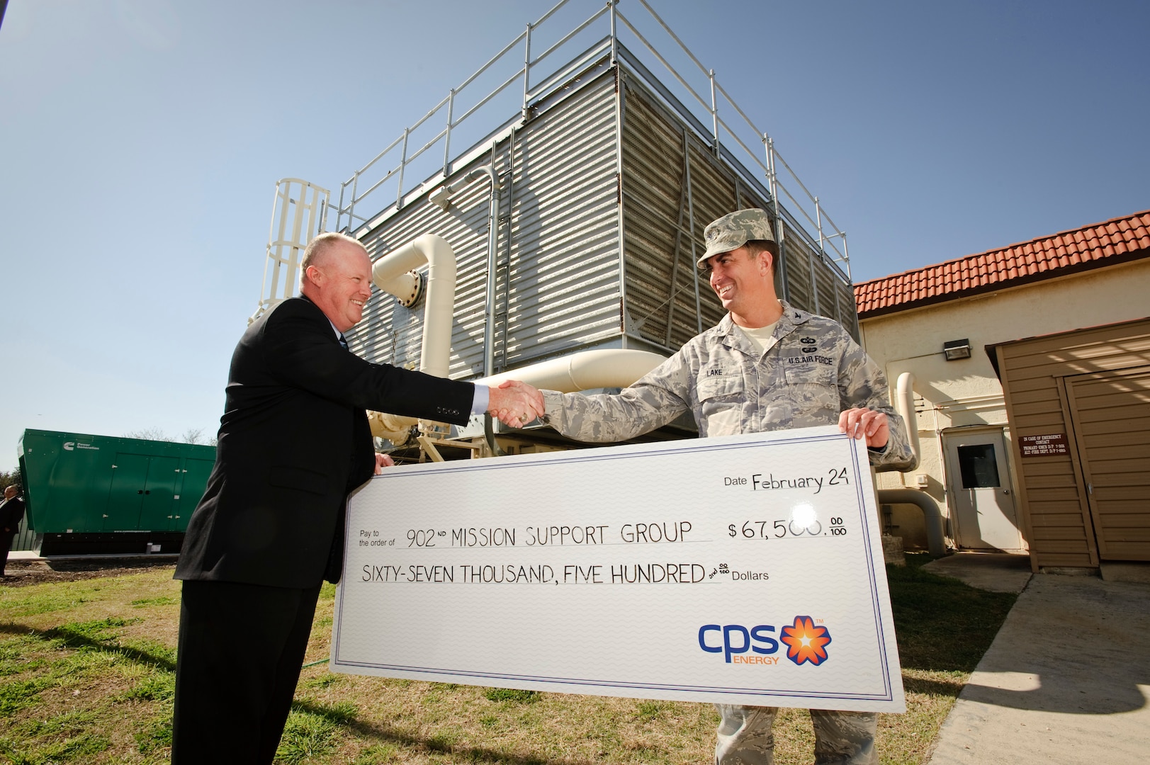 John barrow energy solutions manager for CPS Energy, presents Col. Alan Lake, 902nd Mission Support Group commander, with a check crediting the base utility account for energy savings in front of a newly installed water chilling unit, which will lead to the $67,500 savings in the next year of service. (U.S. Air Force photo/Steve Thurow)