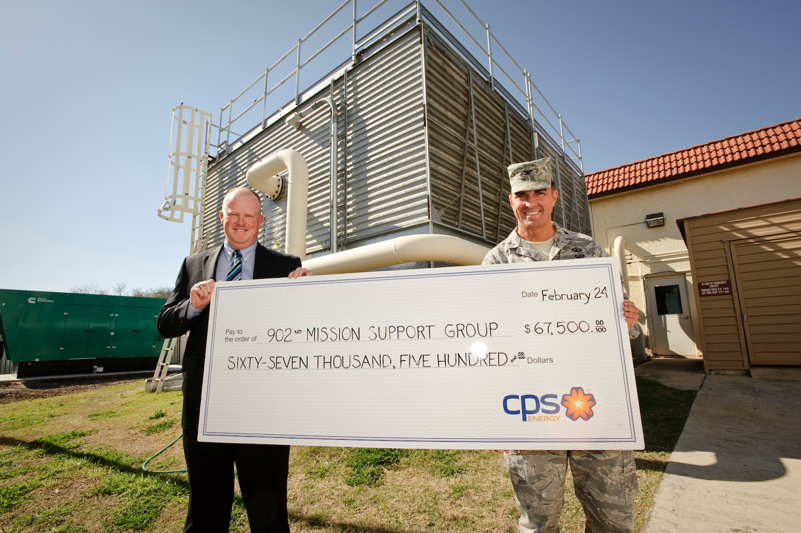 John barrow energy solutions manager for CPS Energy, presents Col. Alan Lake, 902nd Mission Support Group commander, with a check crediting the base utility account for energy savings in front of a newly installed water chilling unit, which will lead to the $67,500 savings in the next year of service. (U.S. Air Force photo/Steve Thurow)