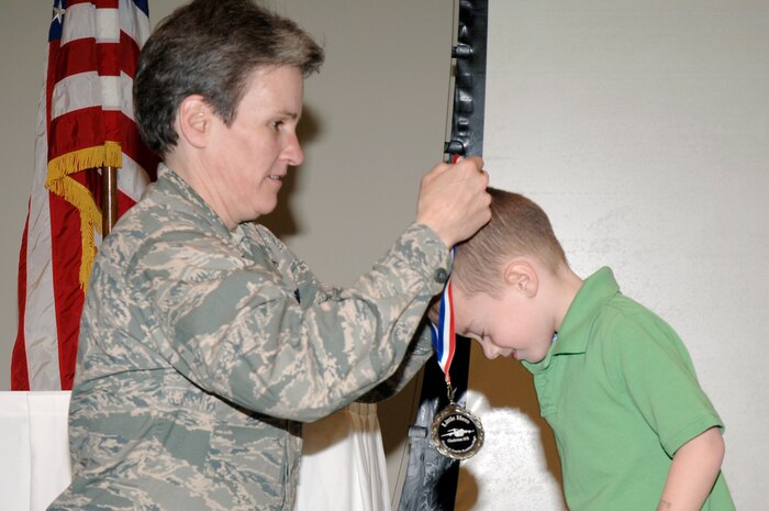 Col. Martha Meeker places a medallion around the neck of Christian Wicker during the Little Heroes ceremony held at the Education and Training Center Feb. 25 at Joint Base Charleston. Little Heroes is a ceremony to recognize children for the sacrifices they made during a parent’s recent deployment. Each child is presented with a medallion with a C-17 imprinted on the face and a certificate signed by the parent’s respective wing commander. Colonel Meeker is the 628th Air Base Wing commander and Christian is the son of Capt. John and Courtni Wicker with the 17th Airlift Squadron. (U.S. Air Force photo/Staff Sgt. Marie Brown/Released)