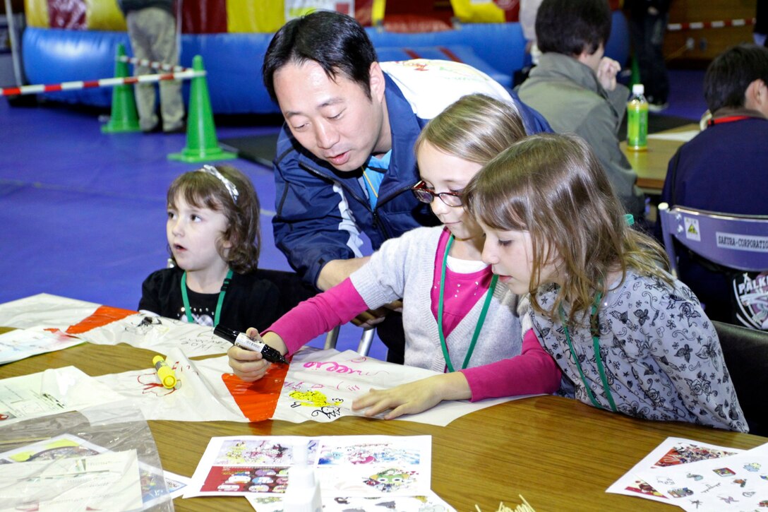 Yoshikiko Fukuda, mayor of Iwakuni,  admires the kites made and designed by Chloe Lawson (left), Millie Lawson (center), and Alaina Lawson (right) during the US-Japan Friendship Exchange at marine Corps Air Station Iwakuni, Japan Feb. 27.  The friendship exchange brought students from M.C. Perry Elementary Schoola nd Kawashimo Elementary School together with a series of activities including kite making, tug-of-war, basketball, dodgeball, and much more.  WIth an opportunity to interact and play, students and their parents were able to share cultural experiences and form a common bond.