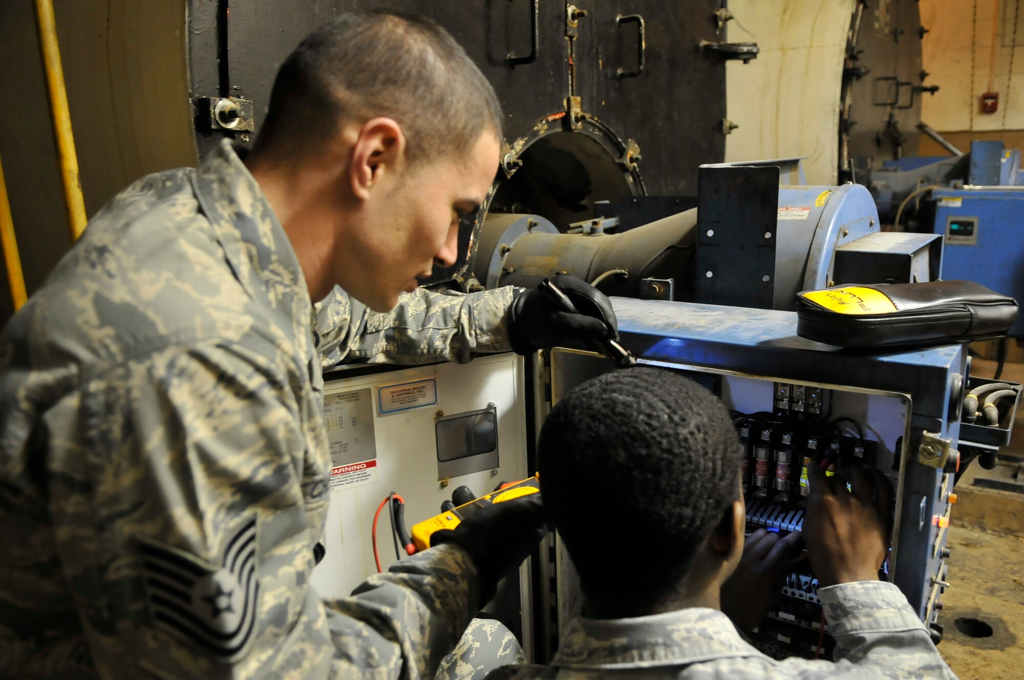 Tech. Sgt. Michael Cherry and Airman 1st Class Jarrett Myles use a multimeter in the boiler room Dec. 21, 2009, on Eielson Air Force Base. They check the voltage on the control panel to electrically troubleshoot boiler circuitry. They are assigned to the 354th Civil Engeneer Squadron heating ventilation air conditioning flight. (U.S. Air Force photo/Airman 1st Class Janine Thibault)