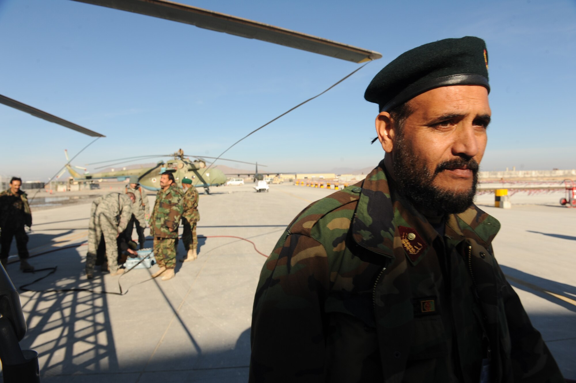 An Afghanistan National Army Air Corps soldier returns to a hanger while his co-workers and Airman perform routine maintenance on an MI-17 helicopter battery at Kandahar Airfield, Afghanistan, Jan. 5, 2010. Airmen attached to the 738th Air Expeditionary Advisory Group provided maintenance training for ANAAC soldiers. (U.S. Air Force photo/Staff Sgt. Manuel J. Martinez/Released)