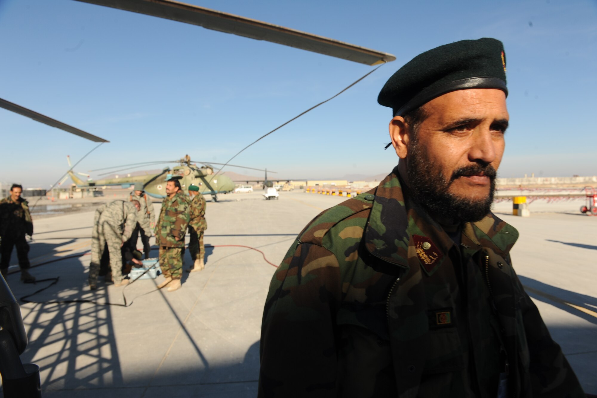 An Afghanistan National Army Air Corps Soldier heads back to a hanger while his co-workers and Airman perform routine maintenance on a Mi-17 helicopter battery Kandahar Airfield, Afghanistan, Jan. 5, 2010. Airmen attached to the 738th Air Expeditionary Advisory Group and provide maintenance mentorship for ANAAC Soldiers. (U.S. Air Force photo by Staff Sgt. Manuel J. Martinez/Released) 