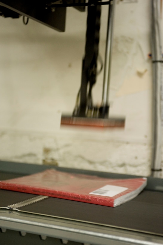 An automated press sticks a mailing label onto a Marine Corps Institute textbook, preparing it for shipment during a mailing run at the MCI warehouse in the Washington Navy Yard in Washington, D.C., Jan 6. The conveyor belt system includes several scanners, which track inventory and sort mail.