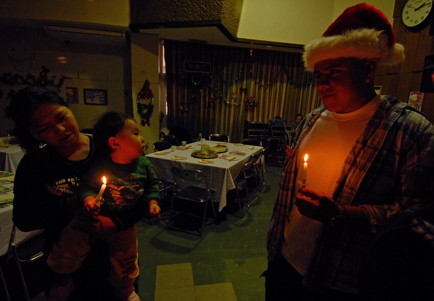 Senior Airman Frank Morales, 18th Communications Squadron, holds a friendship candle with families of the Kadena and Yomitan Lions Club during a holiday party at the Yomitan Social Welfare Center Dec. 19. Half a dozen volunteers representing Kadena handed out more than 150 gifts, several holiday cakes and clothing donations for families of special needs children and adults. (Air Force/Staff Sgt. Jason Lake)