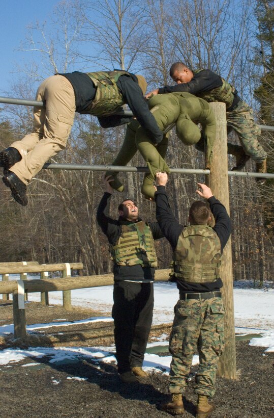Sgt. Steven Richardson (bottom right) and UFC fighter Gabriel Gonzaga (bottom left) pass up a practice dummy to Sgt. Shurron Thompson (top right) and UFC fighter Marcus Davis in an effort to complete an obstacle as a team.  The UFC is teaming up with the Marine Corps in a partnership that will highlight the organizations’ shared values and promote opportunities available in the Marine Corps.