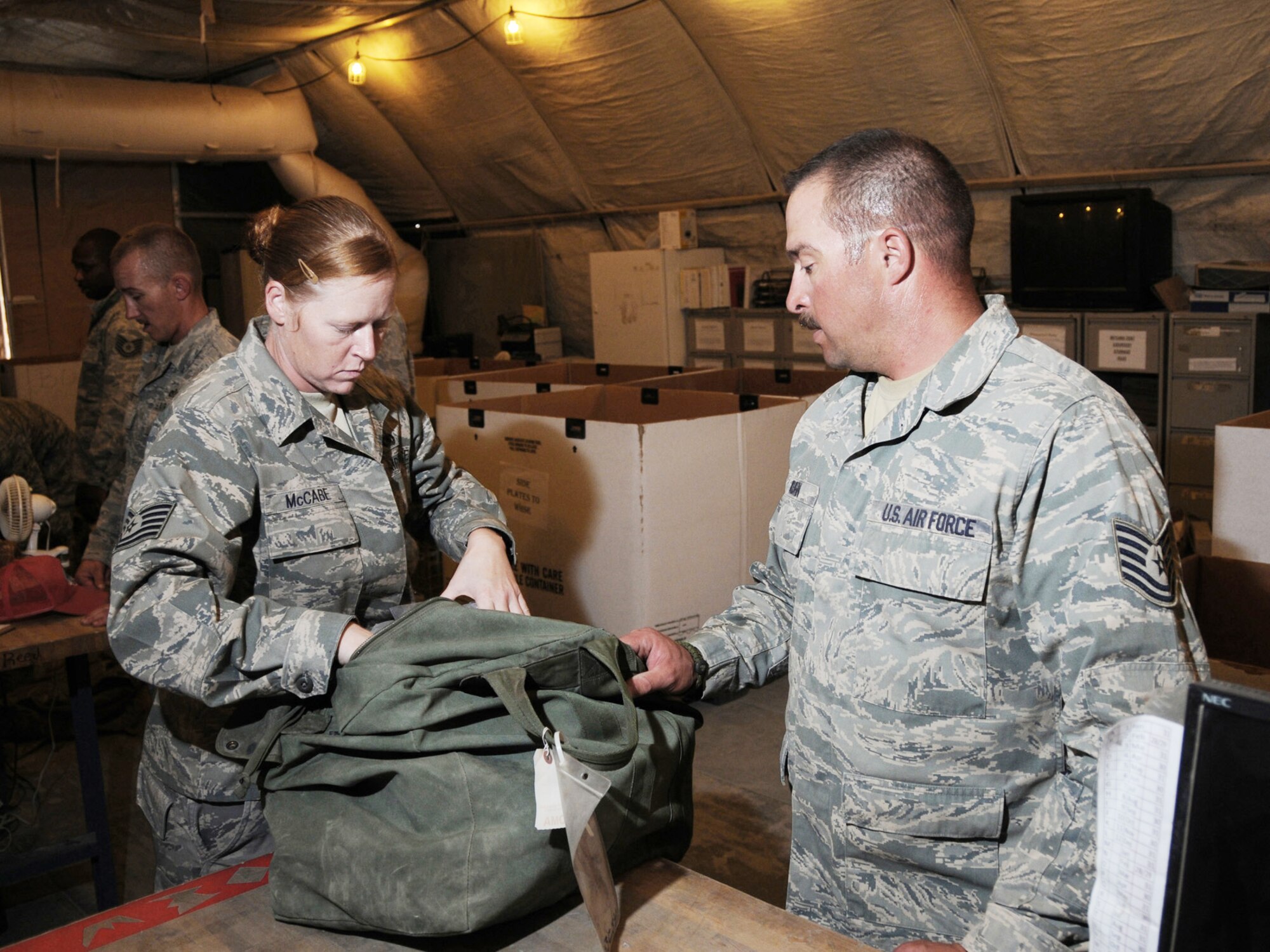 Tech. Sgt. Tina McCabe, 379th Expeditionary Logistics Readiness Squadron expeditionary theater distribution center turn-in tent receives personal mobility gear from Tech. Sgt. Casey Kuhn, 809th Expeditionary Red Horse Group as he passes through on his way home here, Oct. 1.The ETDC turn-in tent recieves mobility equipment from transient personnel as they re-deploy from forward bases. Sergeant McCabe is deployed from Langley Air Force Base, Va. Sergeant Kuhn is deployed from Malmstrom Air Force Base, Mont. Both are deployed in support of Operations Iraqi and Enduring Freedom. (U.S. Air Force Photo/Tech. Sgt. Jason W. Edwards)