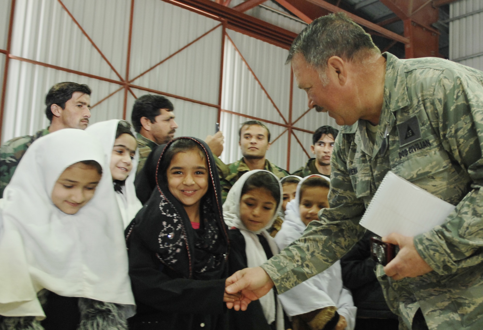 A young Afghan girl smiles as she is greeted by Dr. Charles E. Merkel, Jr., 451st Air Expeditionary Wing historian, at the Afghanistan National Army Air Corps hangar on Kandahar Airfield Dec. 31, 2009.  Dr. Merkel provided a truckload of several boxes of school supplies and candy that had been donated by groups and individuals from the United States and by Airmen from the 451st Air Expeditionary Wing to more than 200 Afghan students. (U.S. Air Force photo by Staff Sgt. Angelique N. Smythe/Released) 