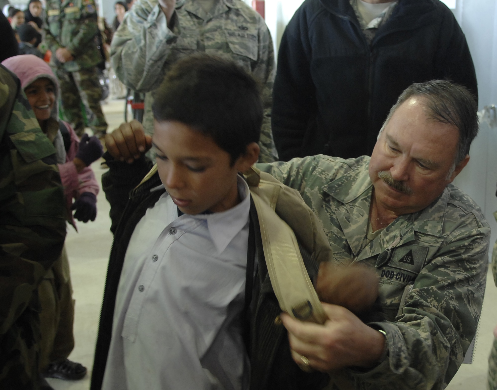 Dr. Charles E. Merkel, Jr., 451st AEW historian, assists a young Afghan boy with his new backpack.  Dr. Merkel donated a truckload of several boxes of school supplies and candy that had been donated by groups and individuals from the United States and by Airmen from the 451st Air Expeditionary Wing to Afghan students who visited the Afghanistan National Army Air Corps hangar on Kandahar Airfield Dec. 31, 2009. (U.S. Air Force photo by Staff Sgt. Angelique N. Smythe/Released) 