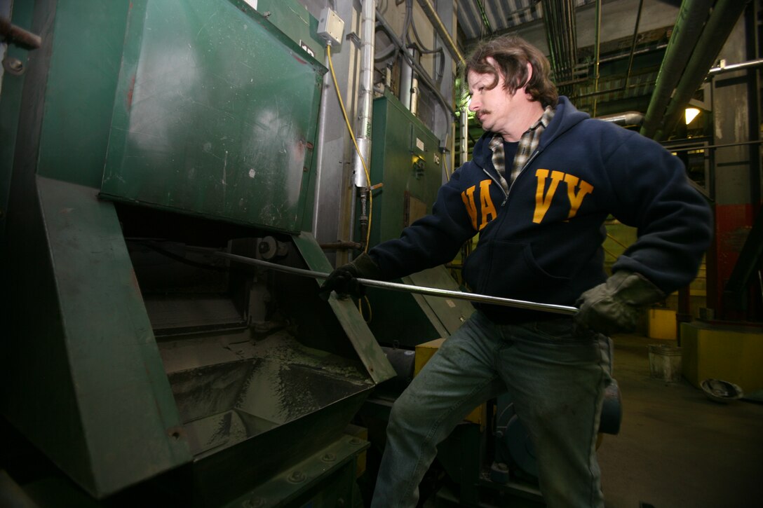 Central heating facility worker Tim Hallman clears ash from an ash hopper to ensure the passageway stays clear of debris. The ash hoppers must be cleared twice every shift.