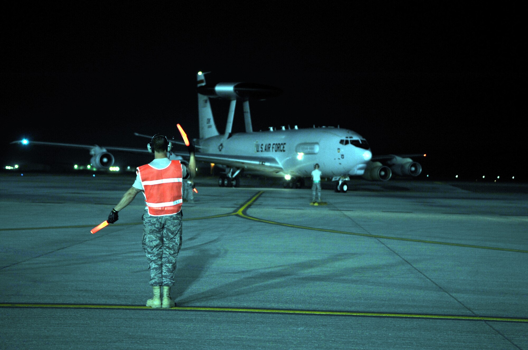 A maintenance Airman waves an E-3 Sentry Airborne Warning and Control System aircraft to come in to park on the flightline of a non-disclosed base in Southwest Asia on Jan. 10, 2010. The aircraft and Airmen, assigned to the 380th Air Expeditionary Wing, support Operations Iraqi Freedom and Enduring Freedom and the Combined Joint Task Force-Horn of Africa. (U.S. Air Force Photo/Tech. Sgt. Scott T. Sturkol/Released)