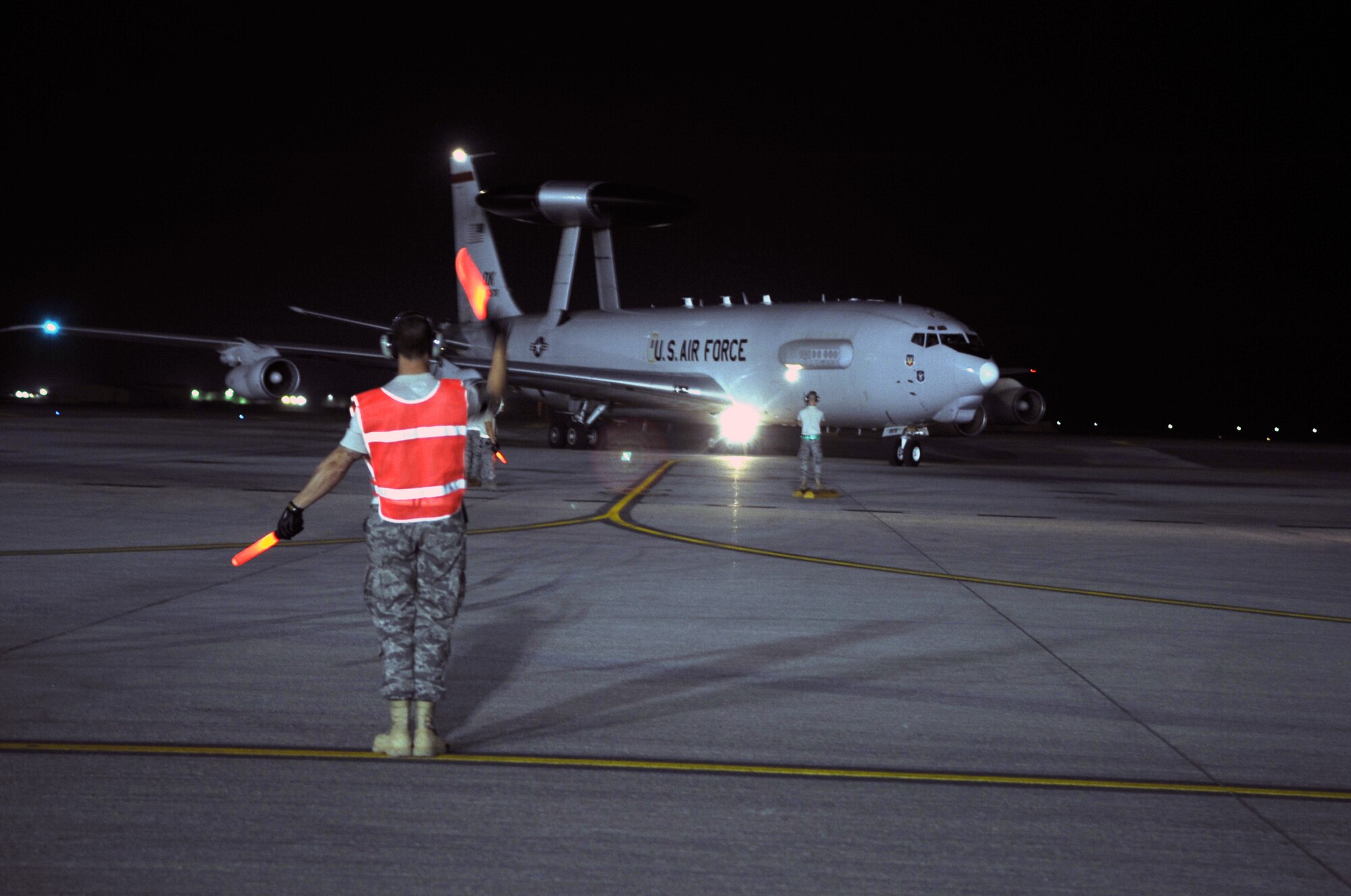 A maintenance Airman waves an E-3 Sentry Airborne Warning and Control System aircraft to come in to park on the flightline of a non-disclosed base in Southwest Asia on Jan. 10, 2010. The aircraft and Airmen, assigned to the 380th Air Expeditionary Wing, support Operations Iraqi Freedom and Enduring Freedom and the Combined Joint Task Force-Horn of Africa. (U.S. Air Force Photo/Tech. Sgt. Scott T. Sturkol/Released)