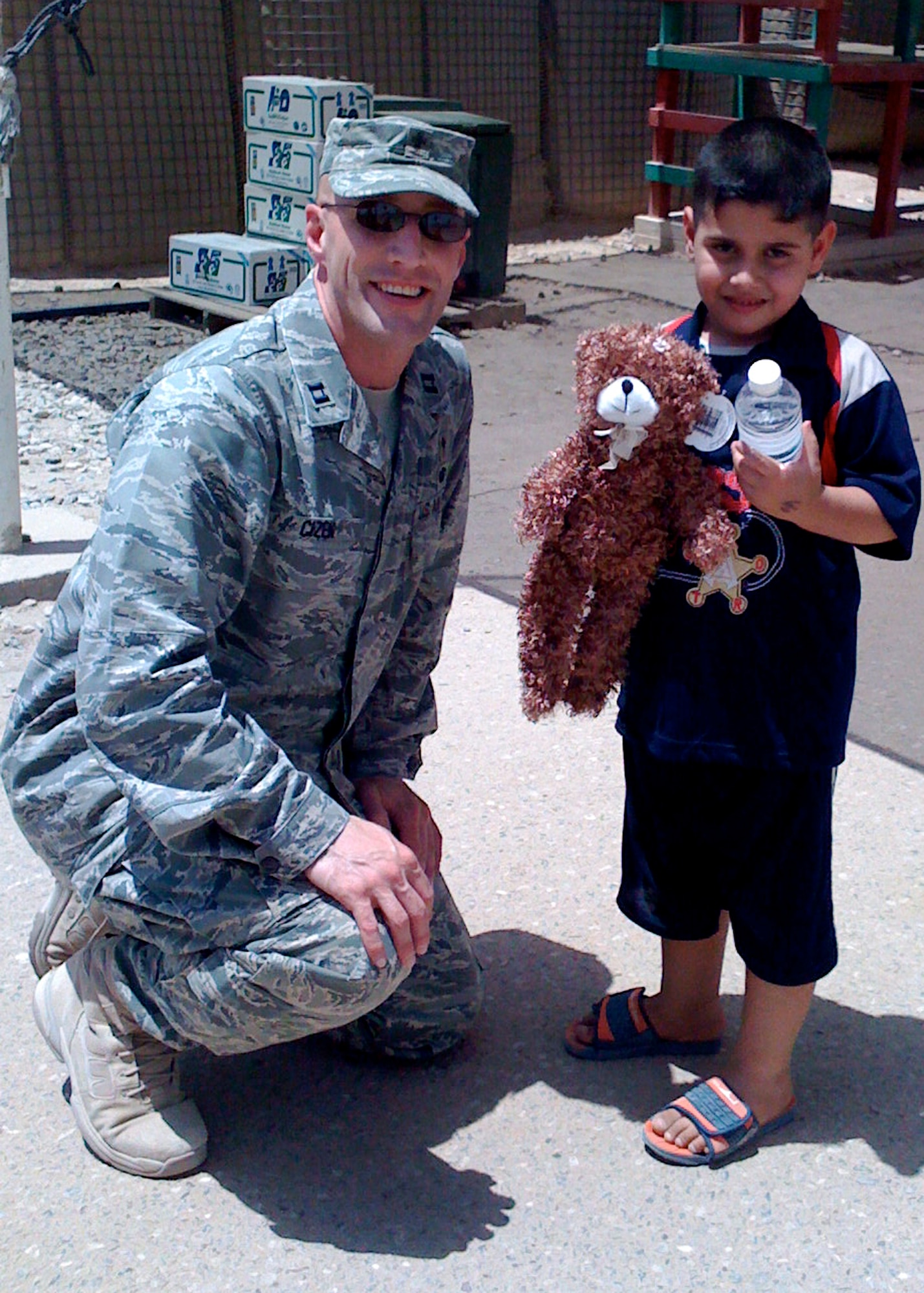 Chaplain (Capt.) Curt Cizek hands out water and a stuffed animal to a local Iraqi boy while deployed to Camp Bucca.  Chaplain Cizek attended to the spiritual needs of the base personnel ranging from all five services, civilian contractors, and third country nationals.