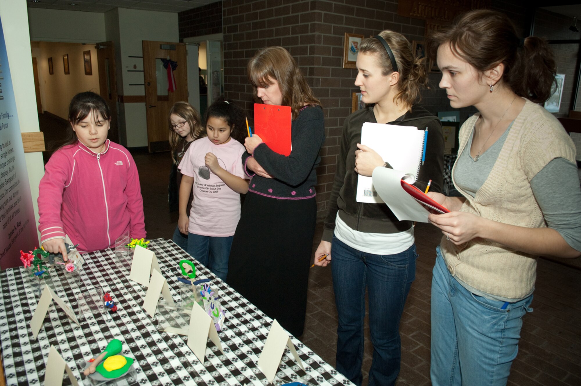 HANSCOM AIR FORCE BASE, Mass. – Tawny Stecher (far left) describes her entry in the Sculpture category to contest judges (right to left) Kelly Latina, Molly Stockwell and Deborah Powers, 66th Force Support Squadron marketing office, in the Hanscom Air Force Base Youth Programs Fine Arts Exhibit. Looking on (foreground) is Jayde Milliman and Arianna Martinez who also competed in this year’s event. First Place category winners included:  Vanessa Martinez - Watercolors category ages 9 and under; Jade Milliman – Multicolored Drawing category ages 9 and under; Thomas Davis – Multicolored Drawings  category ages 13 to 15; Drew Harris – Sculptures category ages 9 and under; and dual category winners Aiyanna Simmons – in Pastels and Acrylic Painting categories for ages 9 and under; and Tawny Stecher – in Pastels and Sculpture categories for ages 10 to 12.   (U.S.  Air Force photo by Rick Berry)

