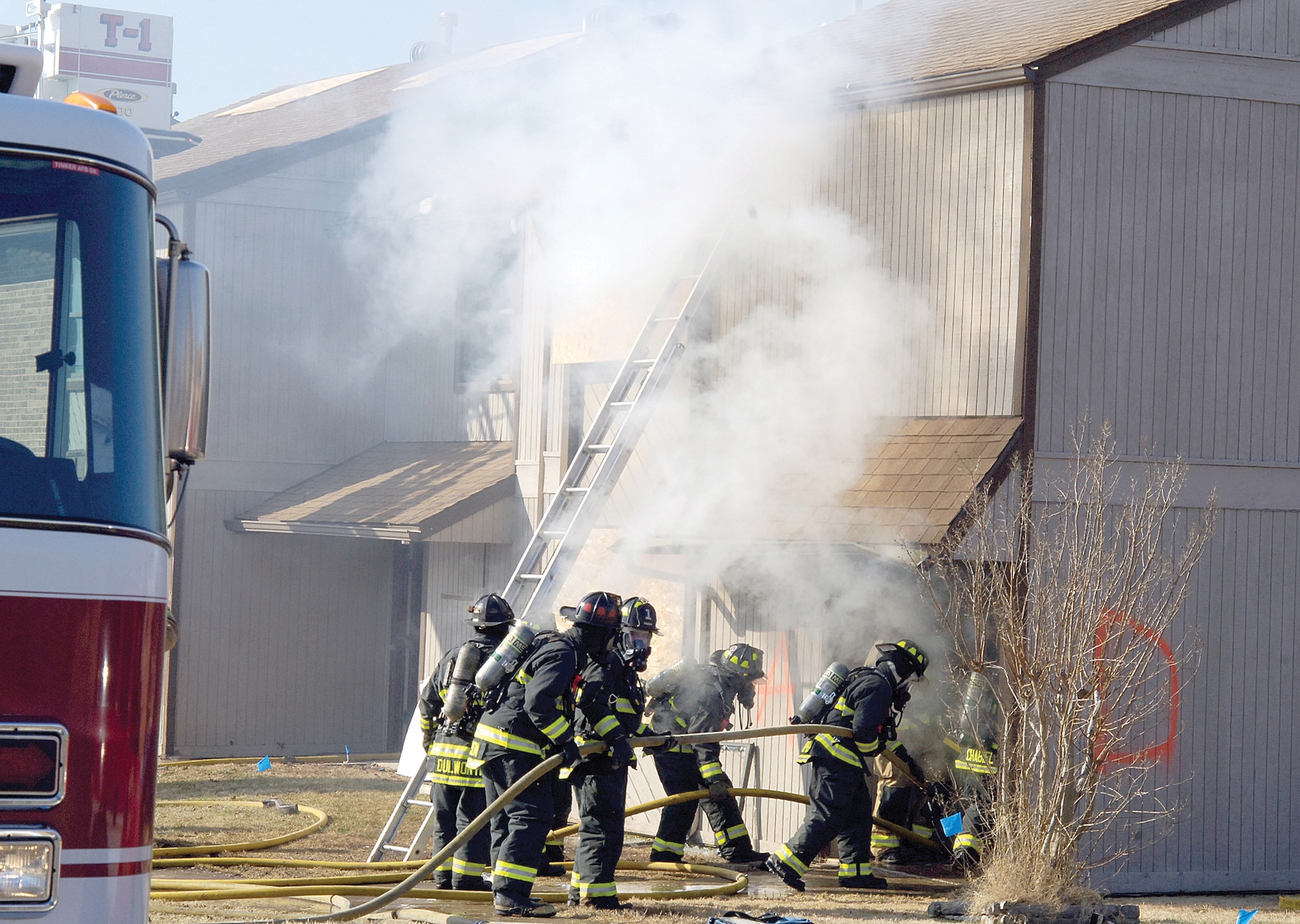 A team advances into the empty Tinker apartment building during the first day of a live-fire training exercise. Four teams attack the fire with different goals, then rotate positions so all can learn and practice what they know.  Teams attack the fire, back up to help protect the first team in, search and rescue and ventilation. Community fire departments also participated in the training. (Air Force photos by Margo Wright)