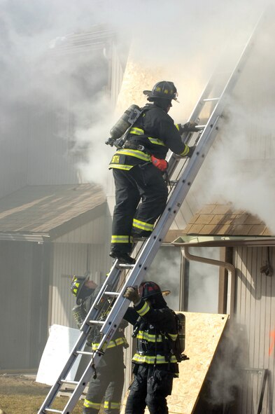 Part of a ventilation team, Tinker firefighter Kevin Smith climbs to the roof of the empty Tinker apartment building during a tightly controlled live-fire training event last week. Empty except for wooden pallets burned in different rooms of the structure, the apartments quickly filled with blinding smoke, heat and flame. While outside temperatures clung to the low teens, the controlled burn soared inside temperatures to 800 degrees. (Air Force photos by Margo Wright)