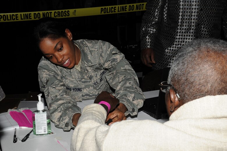 JOINT BASE MCGUIRE-DIX-LAKEHURST, N.J. – Airman Zakkiyah Edwards-Young, a Reservist with the 35th Aerial Port Squadron, puts a wrist-band on an evacuee when signing him in to the McGuire Fitness Center shelter Saturday. The shelter is equipped to provide food, medical care, clothes, and phones to communicate with their family and arrange transportation home. (U.S. Air Force photo/Staff Sgt. Danielle Johnson)