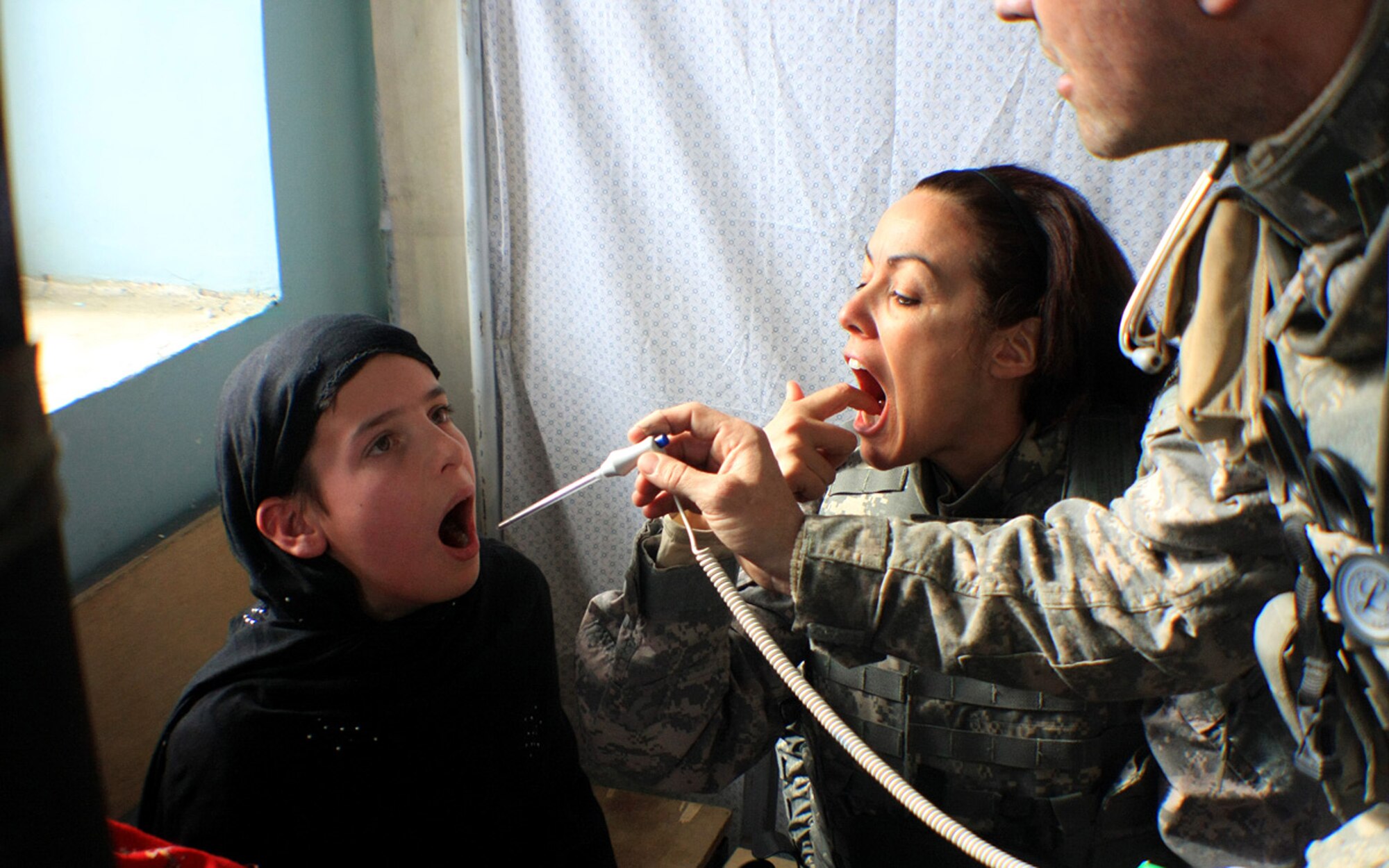 Lt. Col. Montserrat Edie-Korleski shows a young Afghan girl where to hold a thermometer in her mouth as an Army medic treats her Jan. 18, 2009. Colonel Edie-Korleski was deployed to Afghanistan from the Air Force Academy's 10th Medical Group from January to June 2009 and was awarded a Bronze Star medal for her accomplishments downrange. (U.S. Air Force photo)