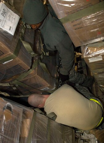 Airman 1st Class Jason Cox, left, and Senior Airman Anel Dominique work to chain down a pallet of food to a McChord AFB C-17 on the Charleston AFB flightline Jan. 18. Sixteen pallets, totaling approximately 116,000 pounds, were loaded on the aircraft with little space between each one, presenting difficulty in securing them to the cargo floor. Airmen Cox and Dominique are air transportation journeyman with the 437th Aerial Port Squadron. (U.S. Air Force photo/Staff Sgt. Daniel Bowles)