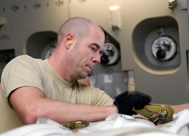 Airman 1st Class Jason Cox tightens down a cargo strap to the top of a pallet of water aboard a McChord AFB C-17 on the Charleston AFB flightline Jan. 18. The strap holds down wooden beams to the top of the pallet, preventing them from injuring passengers or damaging the aircraft during flight. Airman Cox is an air transportation journeyman with the 437th Aerial Port Squadron. (U.S. Air Force photo/Staff Sgt. Daniel Bowles)