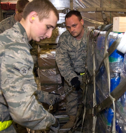 Tech. Sgt. Sean Stottlemyre eyes the progress of Airman Curtis Moore while chaining down a pallet of bottled water to the cargo floor of a McChord AFB C-17 on the Charleston AFB flightline Jan. 18. Chains are used in addition to locks on the cargo floor to inhibit any movement and shifting of pallets during flight. Sergeant Stottlemyre is a night shift supervisor and Airman Moore is an air transportation apprentice, both are with the 437th Aerial Port Squadron ramp services section. (U.S. Air Force photo/Staff Sgt. Daniel Bowles)
