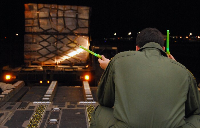 Senior Airman Anthony Jimenez uses a pair of glow sticks to guide the driver of a Tunner 60K Loader aboard a McChord C-17 on the Charleston AFB flightline Jan. 18. The industrial loading vehicle must be carefully positioned to allow expeditious transfer of cargo pallets onto aircraft. Airman Jimenez is a loadmaster with the 10th Airlift Squadron, McChord AFB, Wash. (U.S. Air Force photo/Staff Sgt. Daniel Bowles)