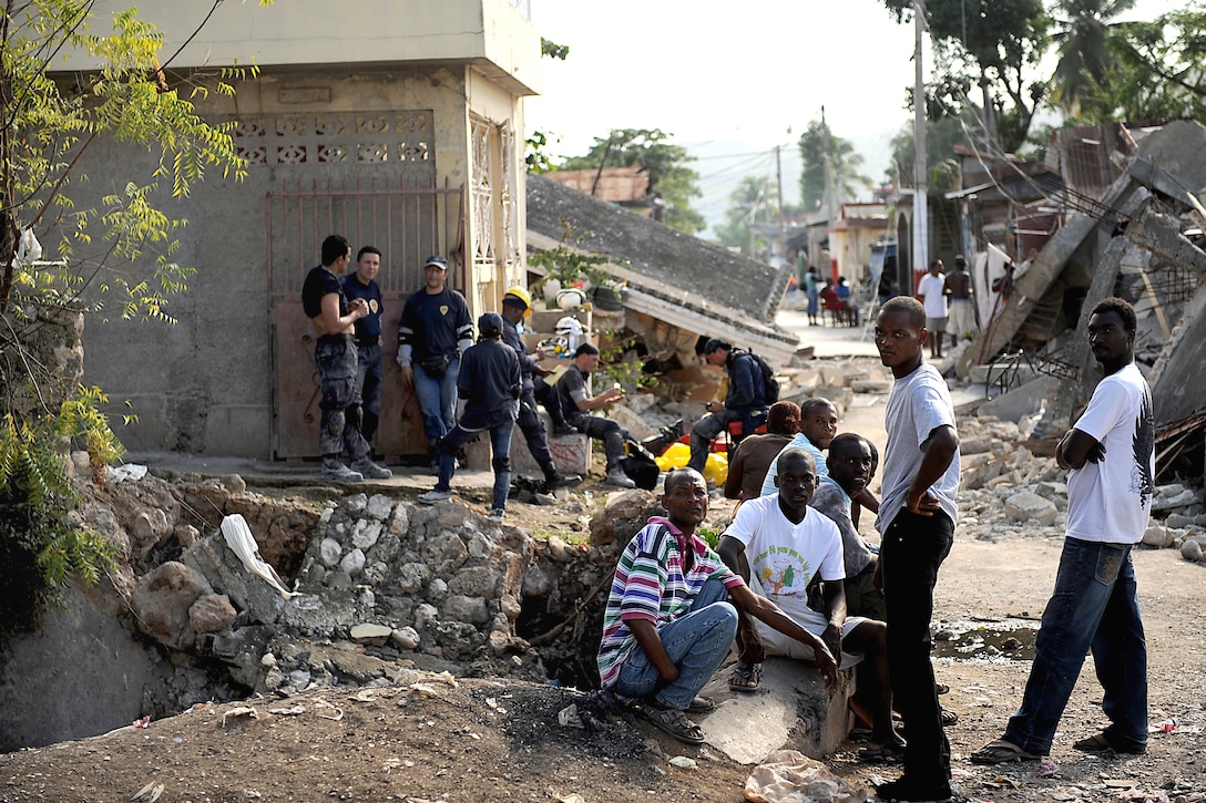 Local residents stand amid destroyed buildings in Jacmel, Haiti, after ...