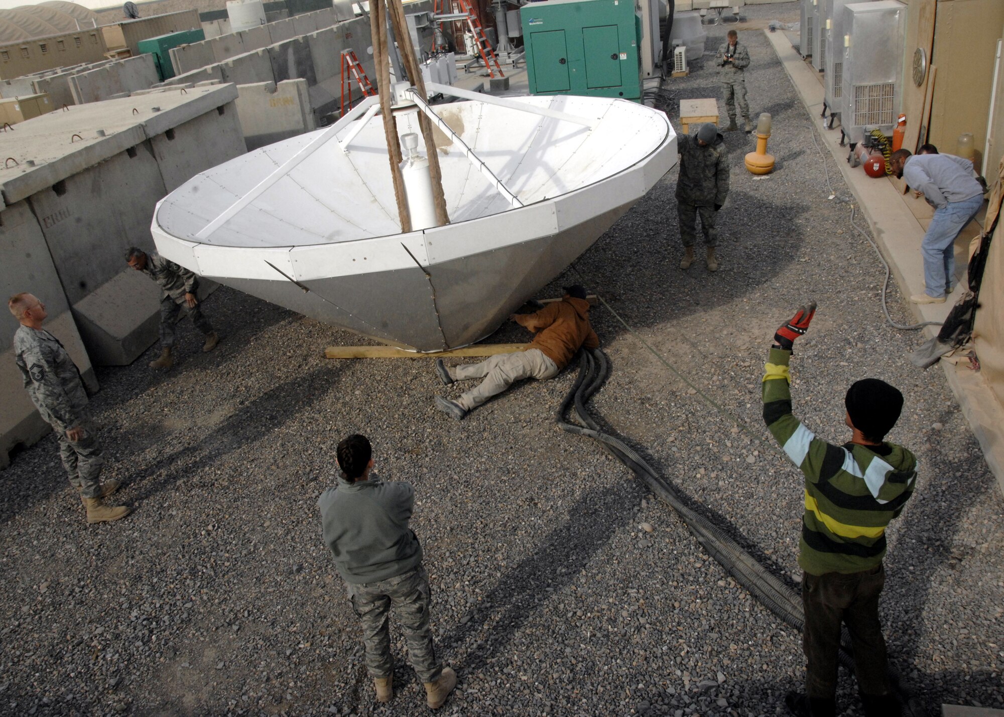 Airmen from the 451st Expeditionary Communications Squadron spot for the crane operator as a satellite dish is lowered onto wooden supports, Jan. 13, 2010. (U.S. Air Force photo/Senior Airman Timothy Taylor/Released)
