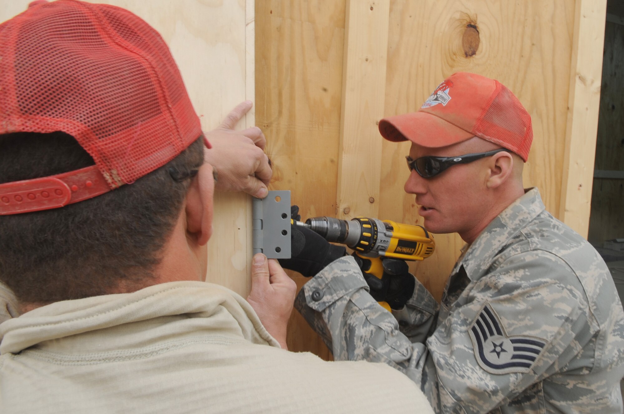 Staff Sgt. Dustin Holmes from the 557th Expeditionary Red Horse Squadron drills a door hinge to the wall during the construction of a badging office on Joint Base Balad, Iraq, Jan. 13, 2010. Red Horse Airmen constructed the office from the ground up, everything from paving the concrete to building the wood-frame and installing the interior finishes. (U.S. Air Force photo/Senior Airman Brittany Y. Bateman/Released)