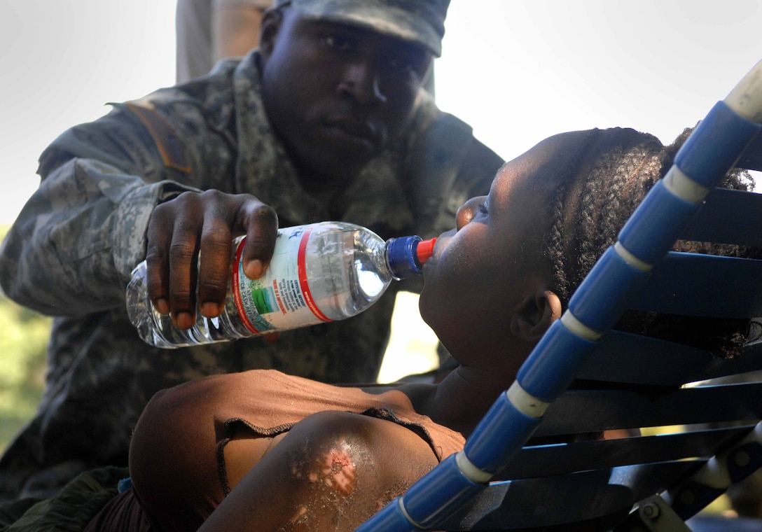 U.S. Army Staff Sgt. Junior Florestal gives Haitian local Sonia Catilius a drink of water at the medic station at the forward operating base established by the 82nd Airborne Division's 1st Squadron, 73rd Cavalry Regiment in Port-au-Prince, Haiti, Jan. 18, 2010. Florestal is a cook with the squadron, but is native of Haiti and is working with the medical section as a translator. The patient, Catilius, is Florestal’s cousin.