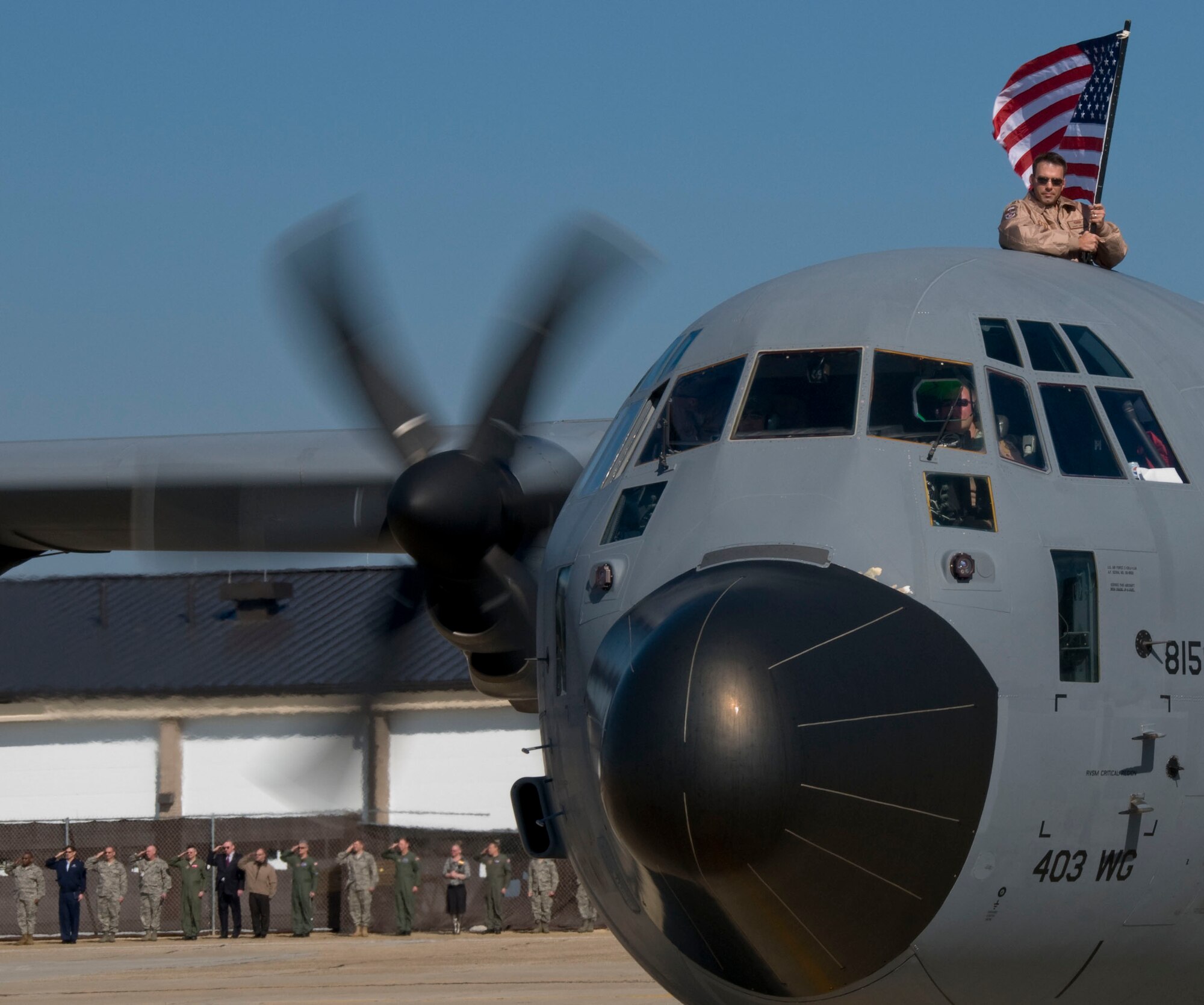 Captain Dave Hogue, intelligence officer of the 403rd Wing, displays the flag while a C-130J-30 carrying returning deployers taxis the runway at Keesler Air Force Base on Jan. 18, 2010. Capt Hogue was one of more than 150 deployers returning home after a four month deployment to Southwest Asia.