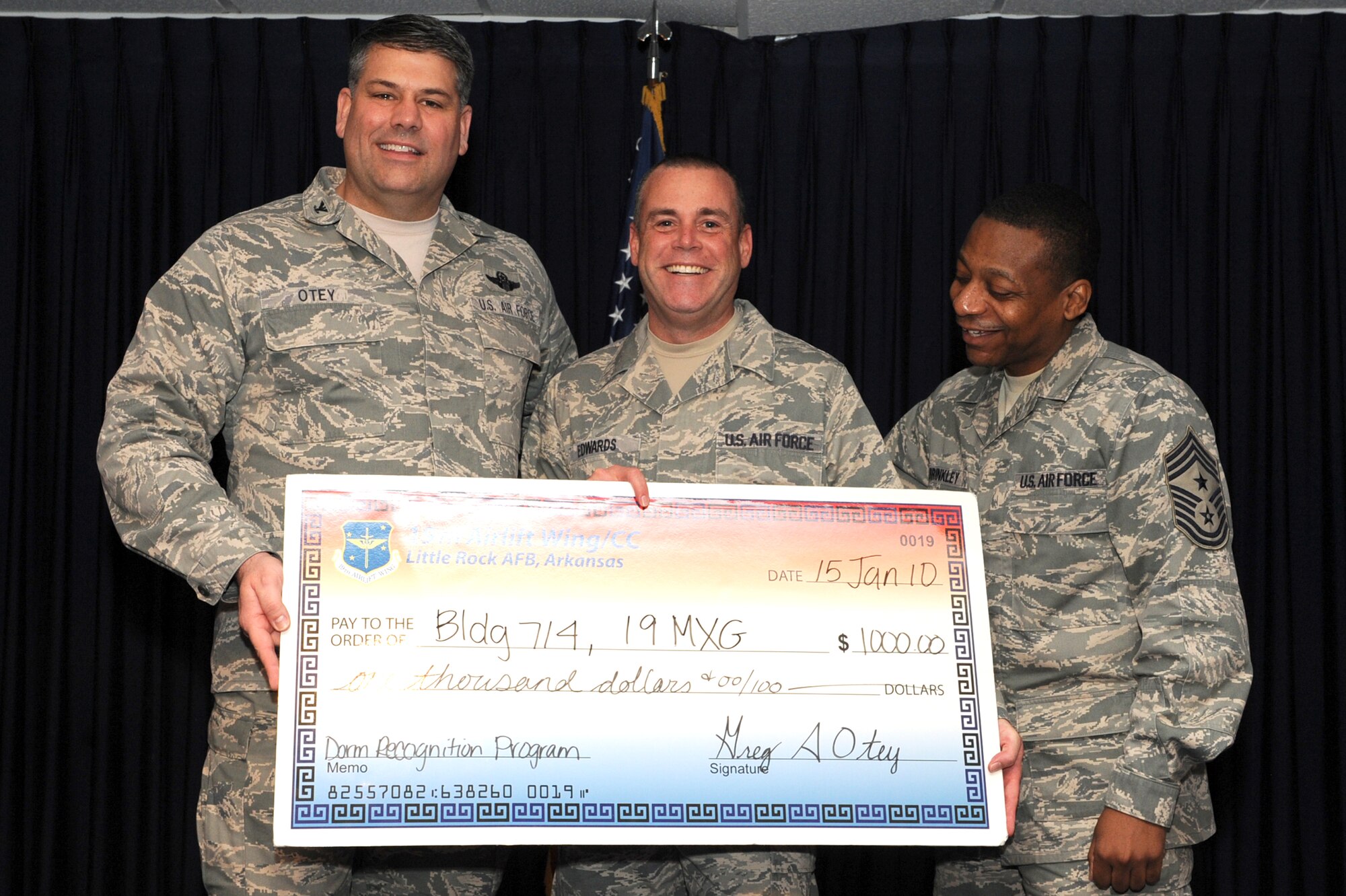 Col. Greg Otey, 19th Airlift Wing commander, and Chief Master Sgt. Anthony Brinkley, 19th Airlift Wing command chief, present Chief Master Sgt. Michael Edwards, 19th Aircraft Maintenance Squadron first sergeant, a $1,000 check for Bldg. 714 Jan. 15 at Hangar 1080. The dorm received the check for winning the quarterly dorm recognition program. (U.S. Air Force photo by Senior Airman Ethan Morgan)