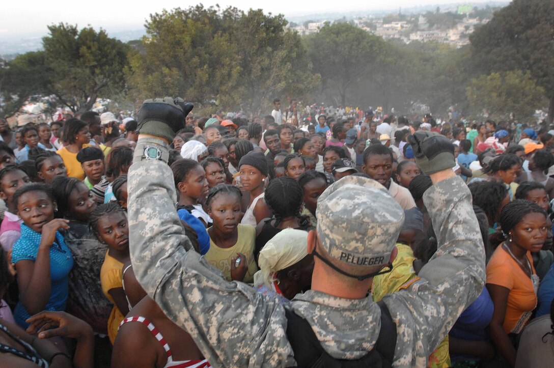 U.S. Army Pfc. Jonathan Pflueger holds his hands above a crowd of women to try to get them to sit down at a humanitarian aid distribution point in Port-au-Prince, Haiti, Jan. 19, 2010. The 82nd Airborne's 1st Squadron, 73rd Cavalry Regiment, provided security for the distribution point out of its make-shift forward operating base.