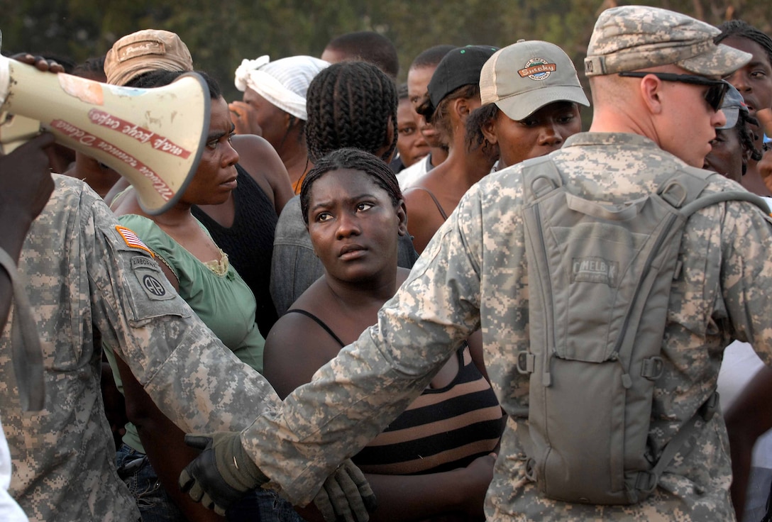 U.S. Army Sgt. Michael Raymond, right, and Sgt. David Huebschman form a human chain to keep the women from trying to rush the humanitarian aid distribution point in Port-au-Prince, Haiti, Jan. 19, 2010. The crowd nearly became uncontrollable as record crowds pushed forward and the food supply dwindled. The 82nd Airborne's 1st Squadron, 73rd Cavalry Regiment, provided security for the distribution point out of its make-shift forward operating base.