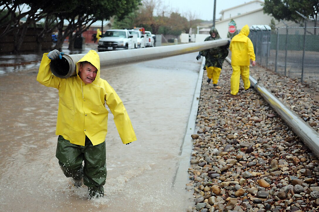 Richard Nixon, boiler technician, and other Base Services Department workers carry pipes down flooded Meyer Avenue at the Marine Corps Air Station in Yuma, Ariz., Jan. 21, 2010. BSD began working early against the storm that dumped more than 2 inches of rain on Yuma by pumping out the excess rainwater to nearby retention basins and Meyer Park. Approximately 4.7 million gallons of water were pumped off station streets and parking lots, according to Jerry Deppen, station facilities maintenance manager.